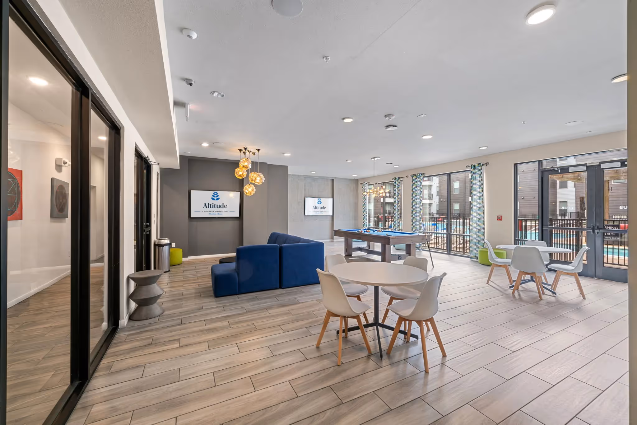 Resident clubhouse with a pool table, lounge seating, and large windows overlooking the pool area at Altitude apartments in Houston, TX.