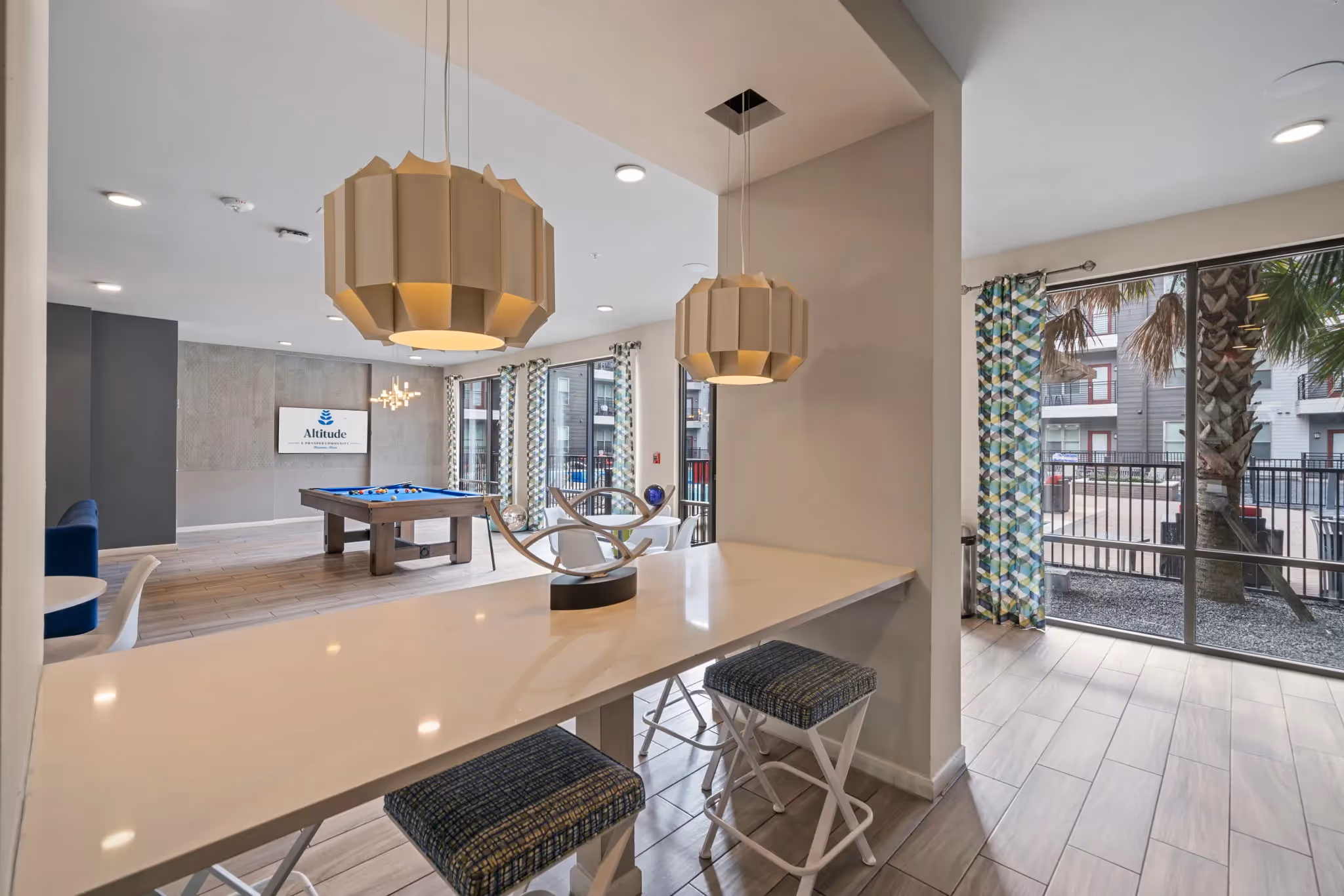 Modern resident lounge with a long bar counter, stylish pendant lights, and pool views, offering a chic social space at Altitude in Houston, TX.