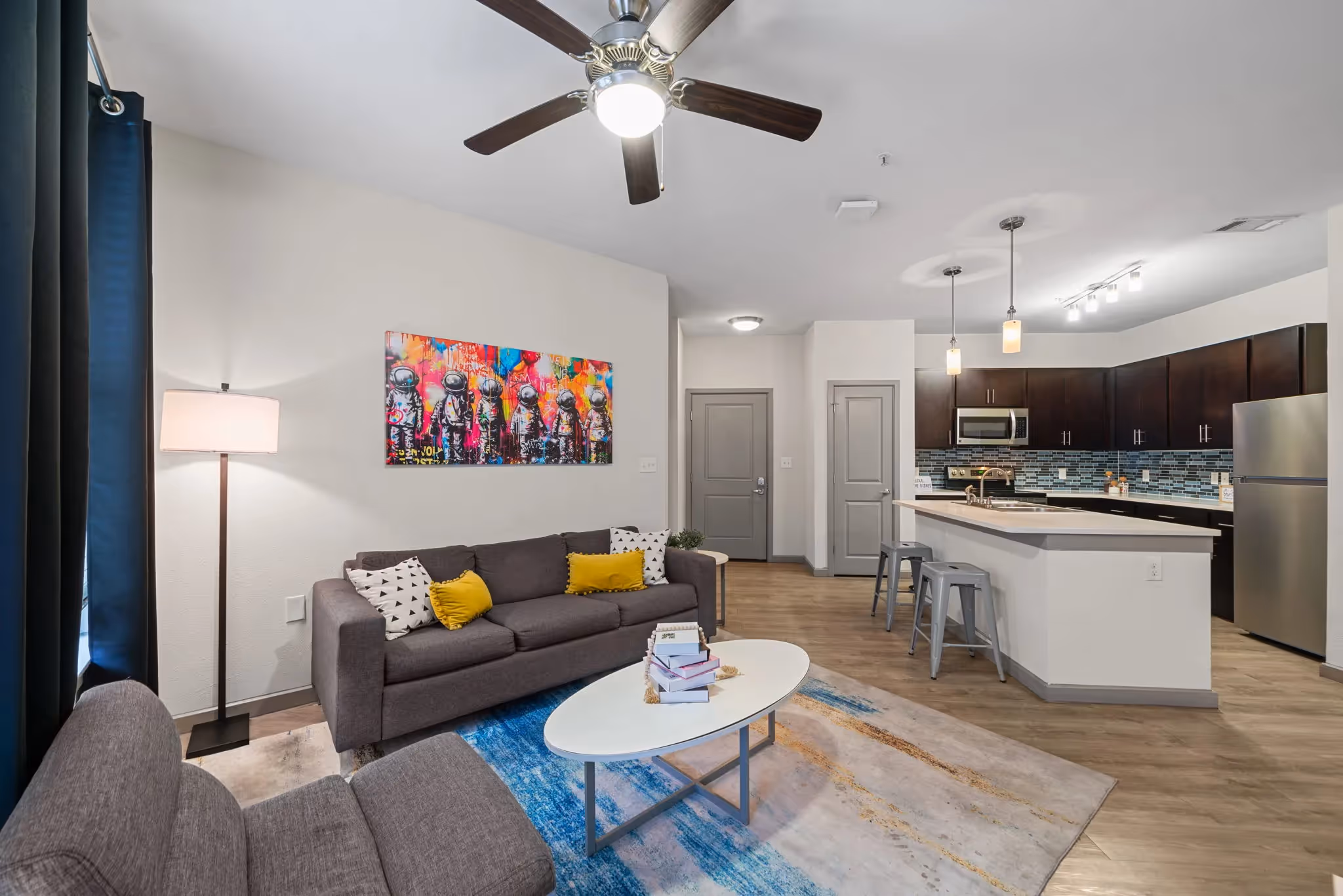 Contemporary living room in an apartment at Altitude in Houston, TX, featuring a grey sofa, colorful art, and an open layout connecting to the kitchen.