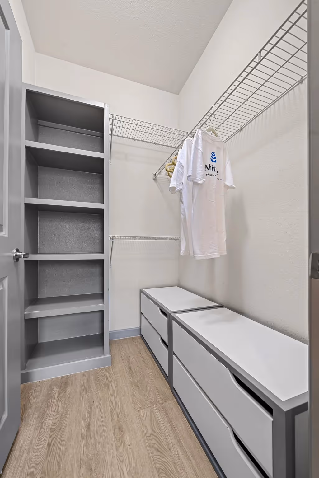 Spacious walk-in closet with built-in shelves and drawers, featuring an Altitude branded t-shirt, in an apartment at Altitude in Houston, TX.