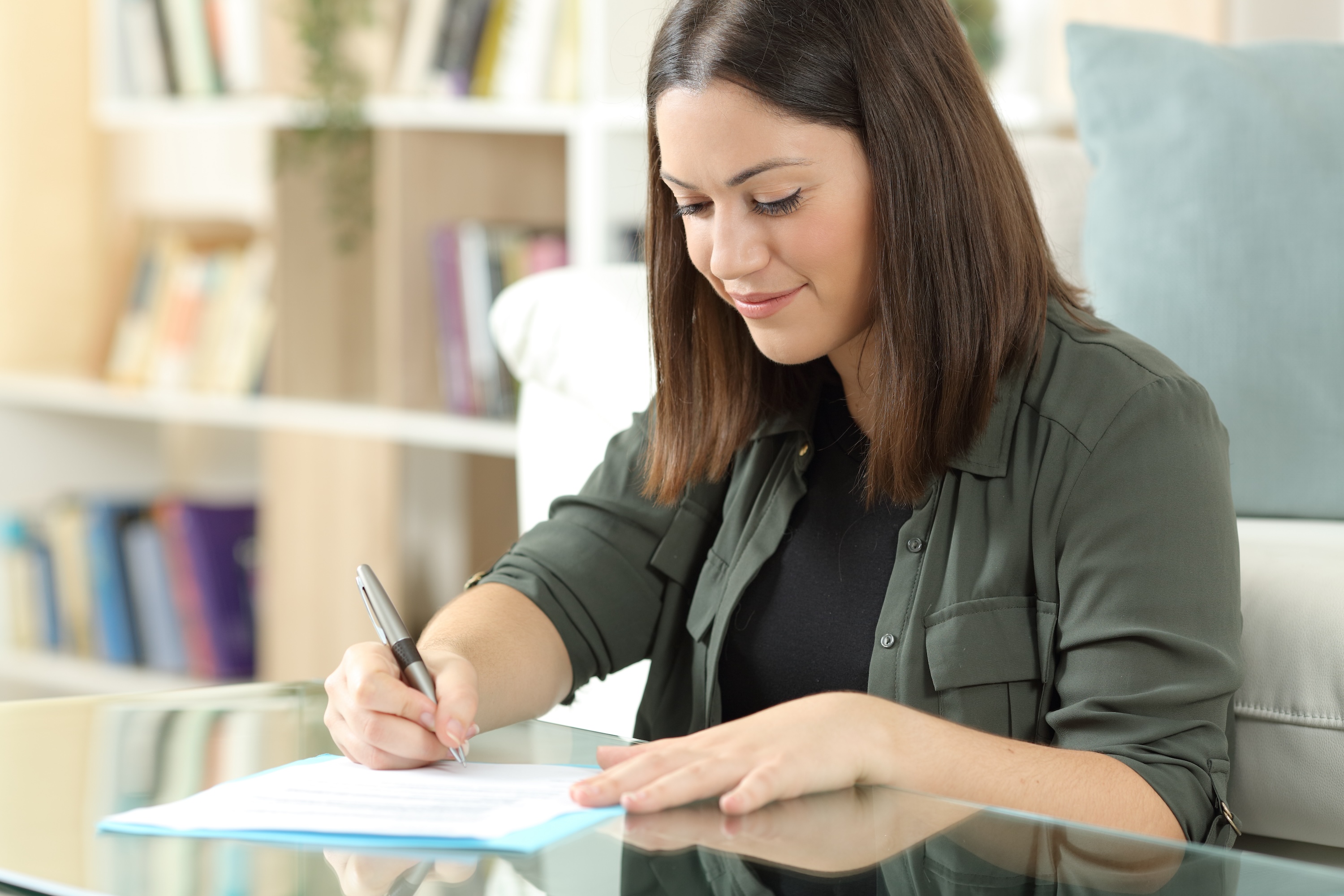 A smiling woman sitting on a sofa and happily filling out paperwork, representing the easy and convenient leasing process at Altitude in Houston, TX.