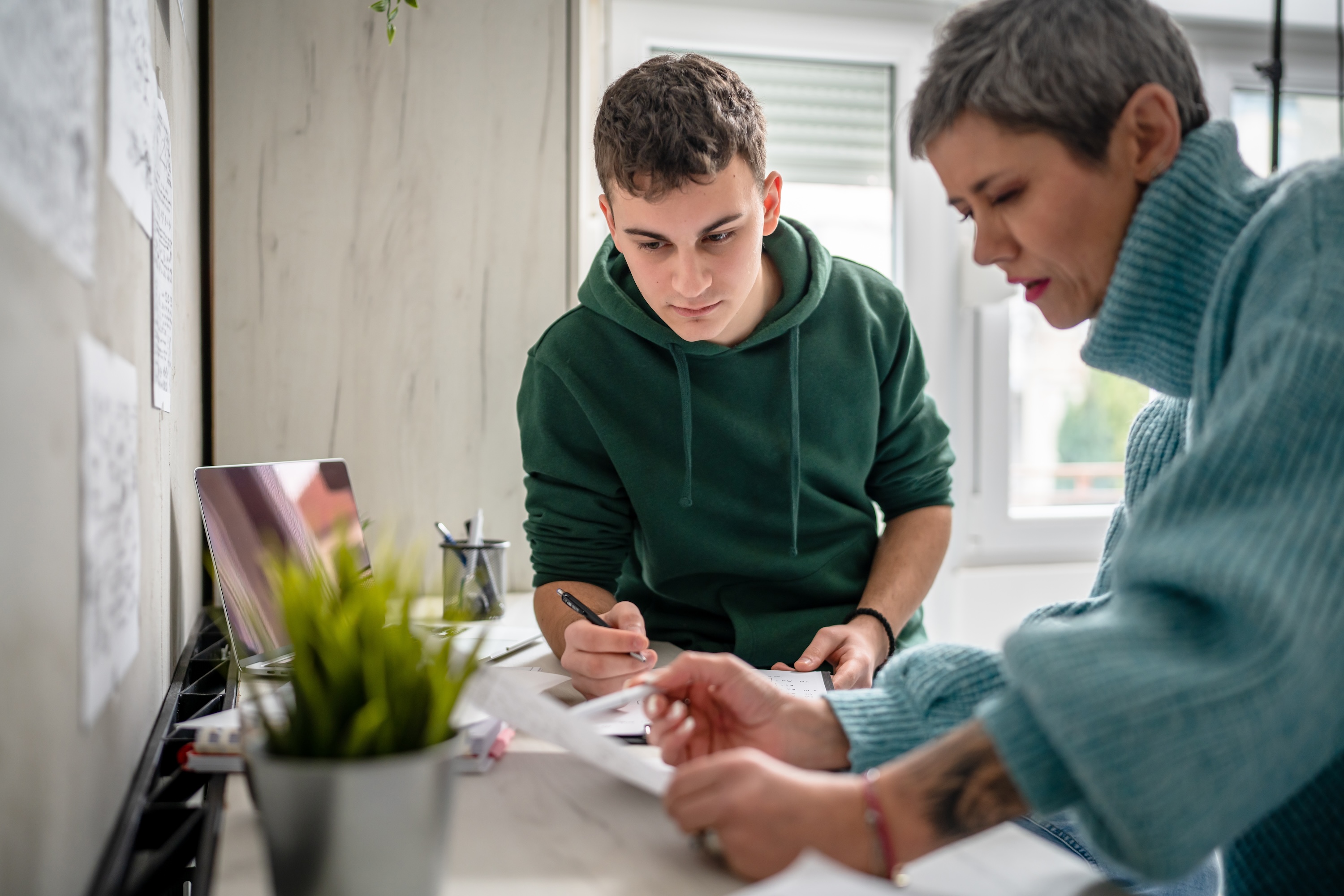 A college student and an adult working together on school paperwork at a desk in a well-lit apartment, representing the ideal study environment at Altitude, a Prosper Community in Houston, TX.