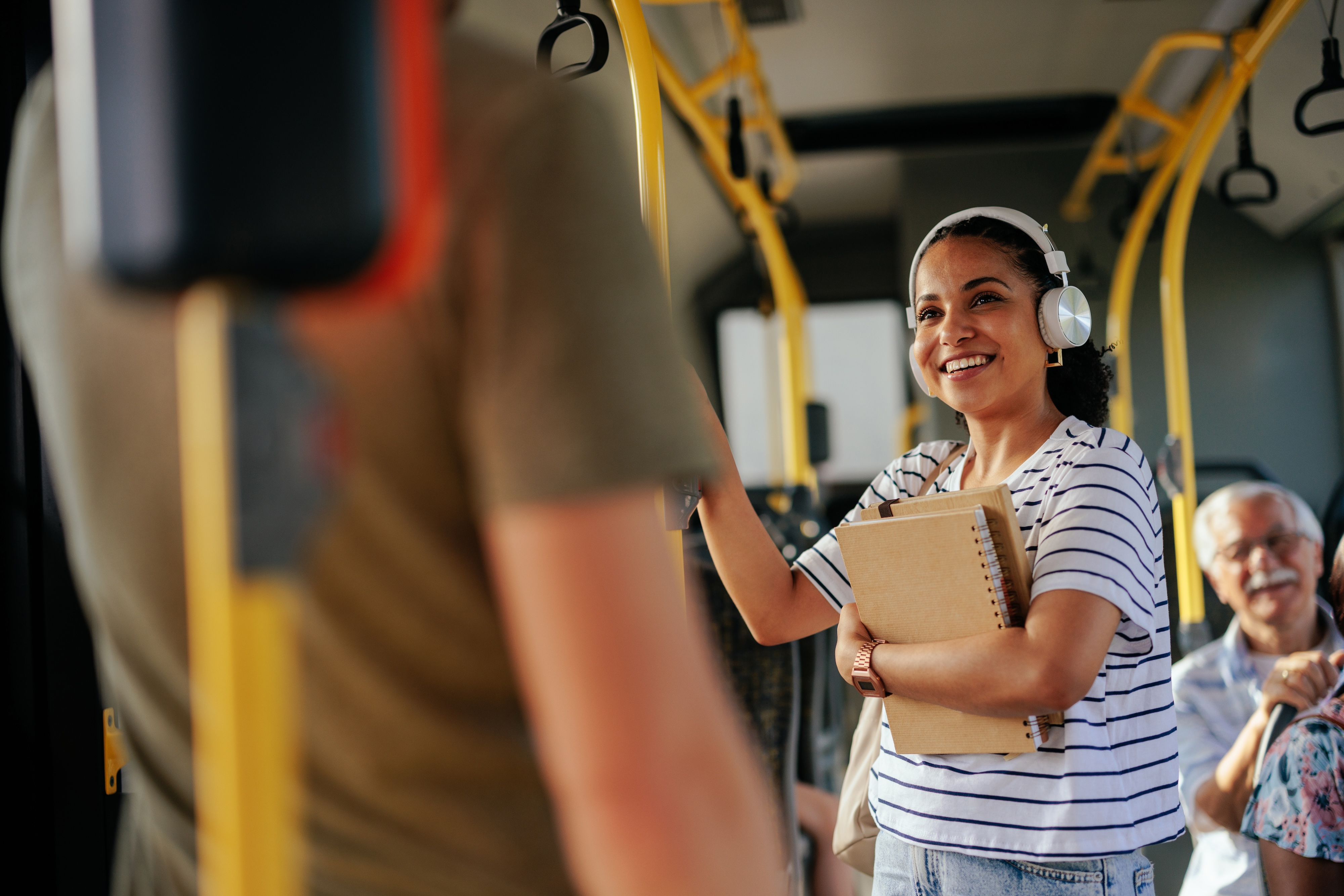 Happy young woman with headphones and notebooks riding a bus, depicting convenient public transportation options near Altitude apartments in Houston, TX.
