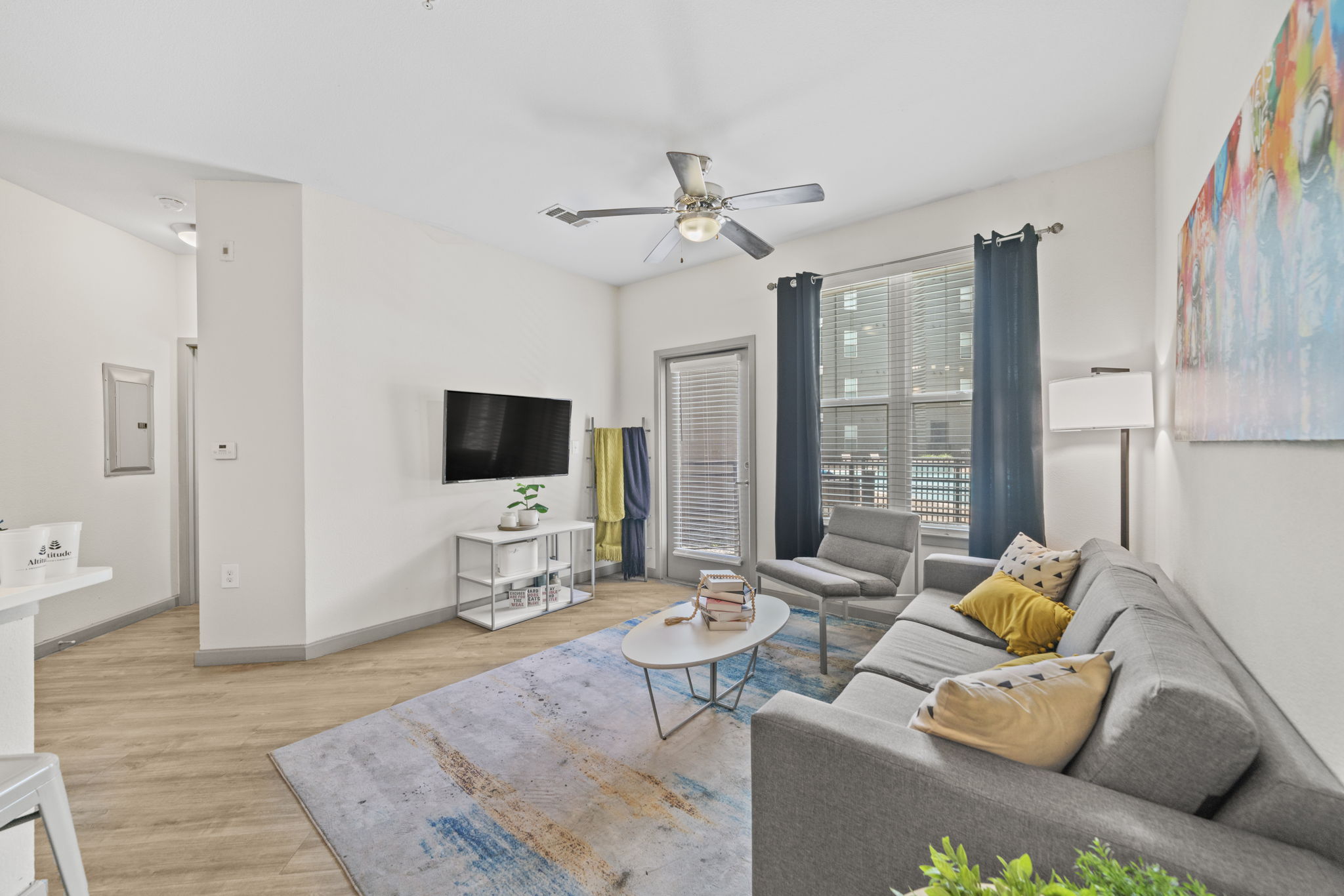 Modern living room with a sofa, TV showing the Altitude logo, and a ceiling fan, showcasing an apartment at Altitude in Houston, TX.