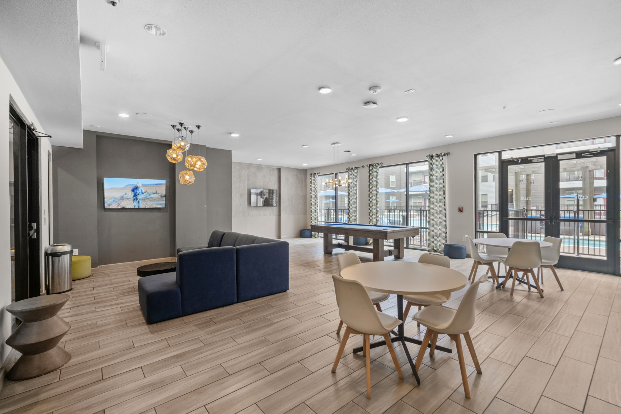 Resident clubhouse with a pool table, lounge seating, and large windows overlooking the pool area at Altitude apartments in Houston, TX.
