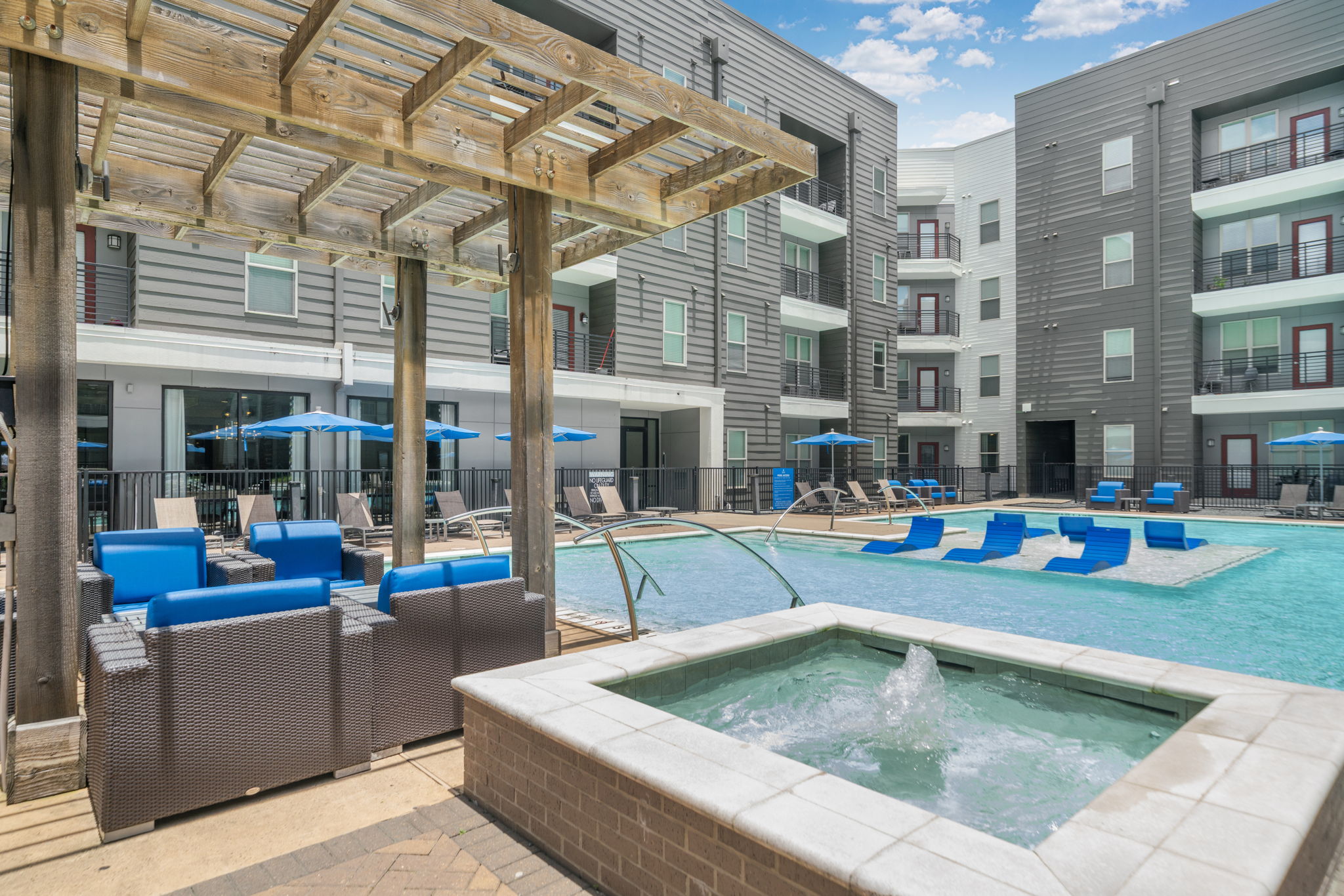 Resort-style swimming pool and hot tub area with lounge seating, surrounded by modern apartment buildings, at Altitude in Houston, TX.