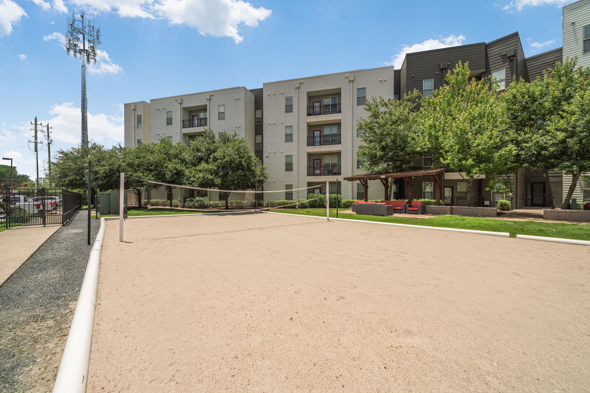 Outdoor sand volleyball court with apartment buildings and a communal lounge area in the background, providing recreational amenities at Altitude in Houston, TX.