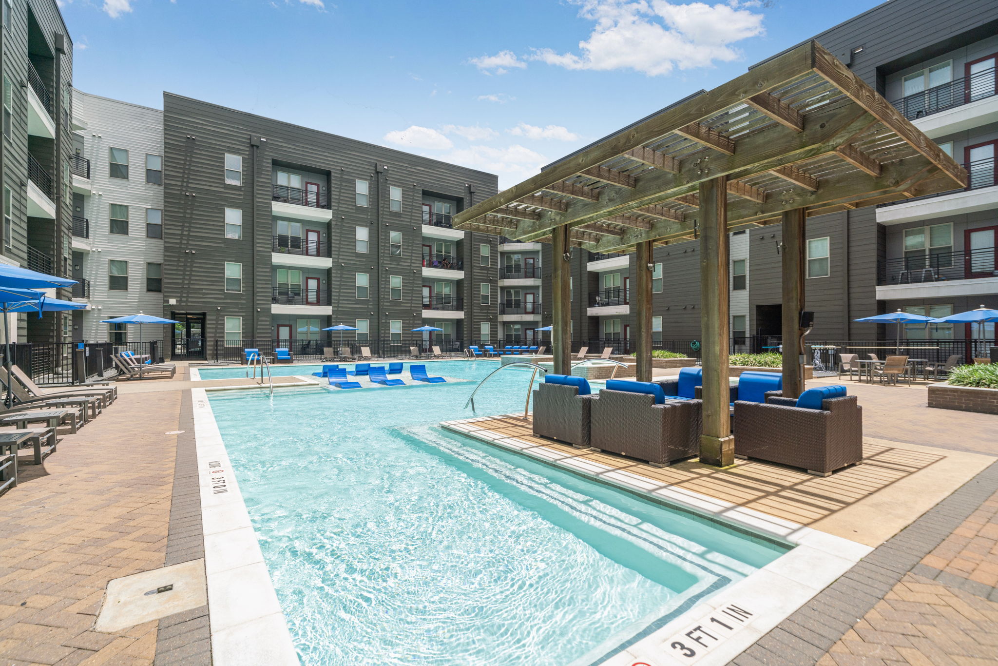 Resort-style swimming pool area with a wooden pergola, lounge chairs, and modern apartment buildings, offering a vibrant outdoor space at Altitude in Houston, TX.