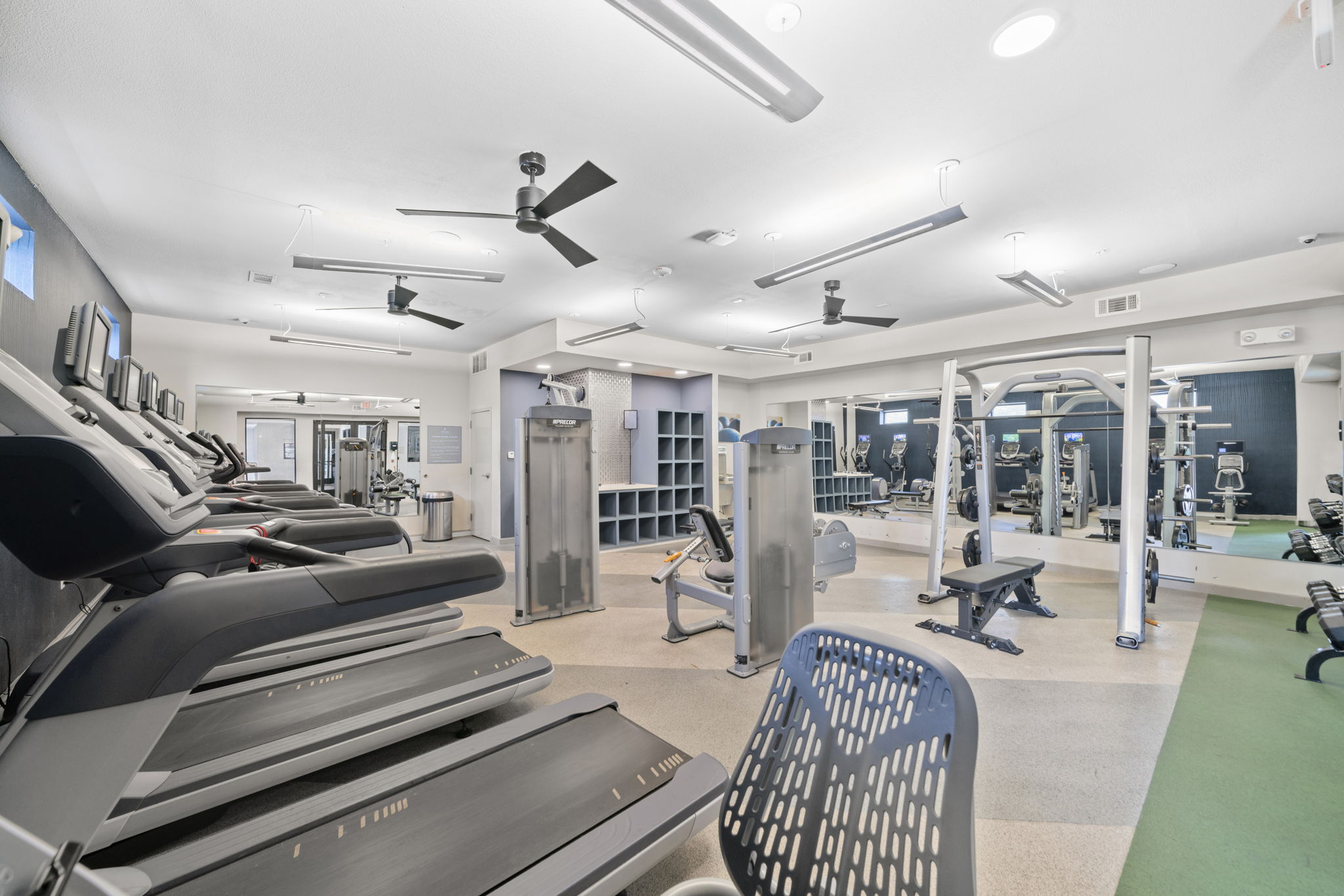 Spacious fitness center with various cardio machines like treadmills and ellipticals, and a distinctive blue accent wall, available to residents at Altitude in Houston, TX.