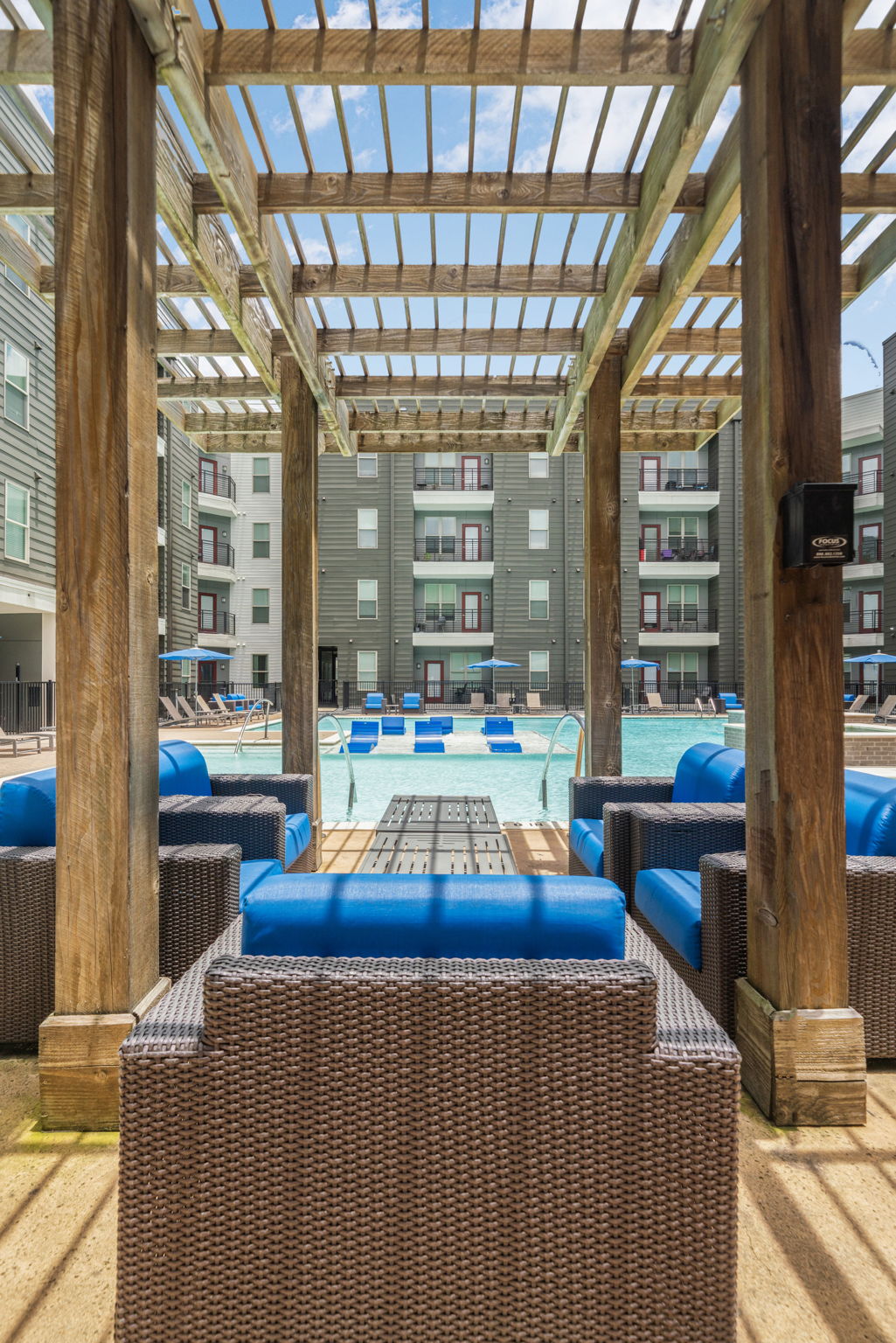 Resort-style swimming pool area with a wooden pergola, lounge chairs, and modern apartment buildings, offering a vibrant outdoor space at Altitude in Houston, TX.
