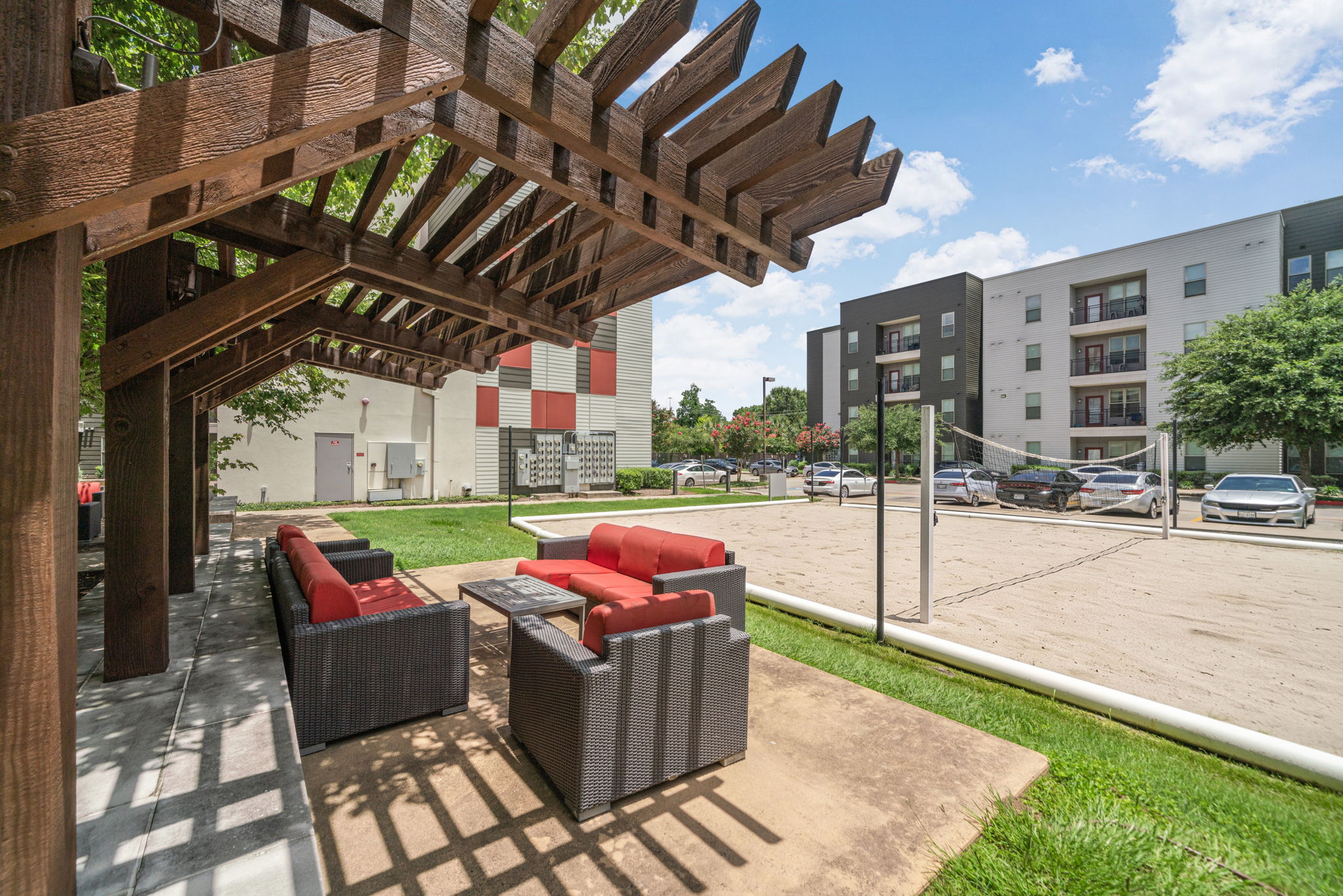 Outdoor sand volleyball court with apartment buildings and a communal lounge area in the background, providing recreational amenities at Altitude in Houston, TX.