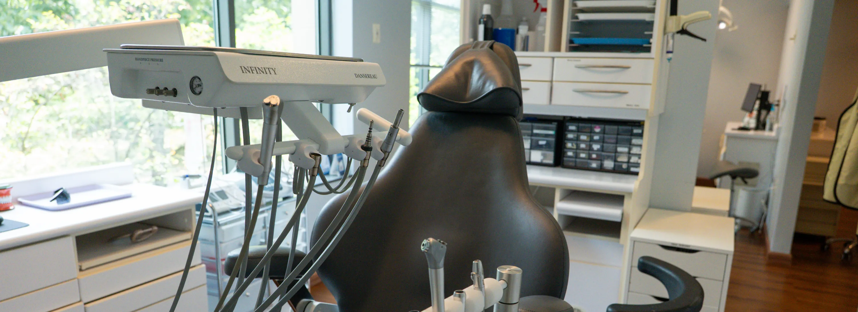 Empty dental chair with attached dental instruments in a modern clinic room with cabinets.