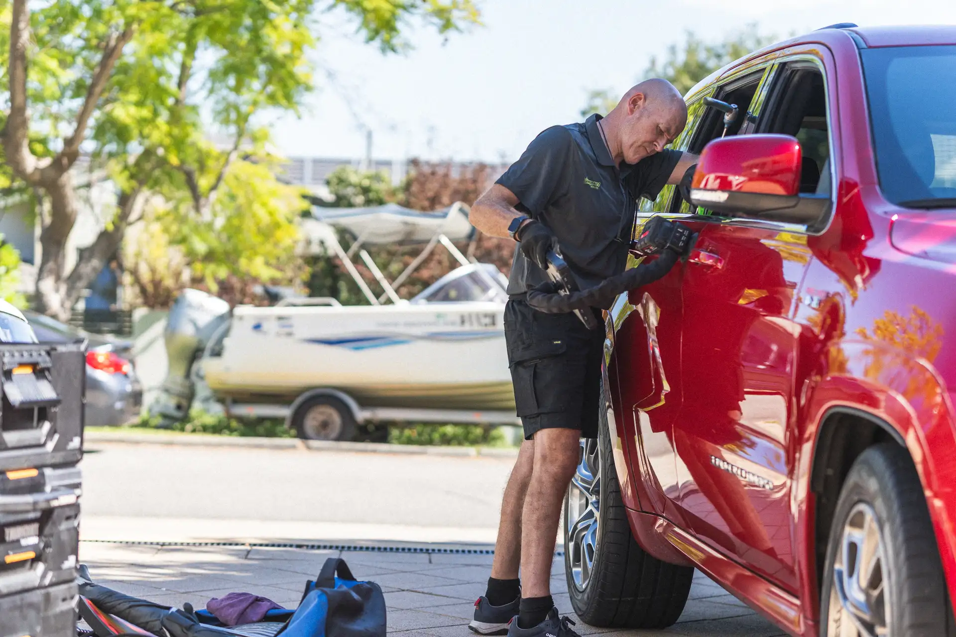 A mobile dent repair technician working on the door panel of a red ute in a Perth driveway