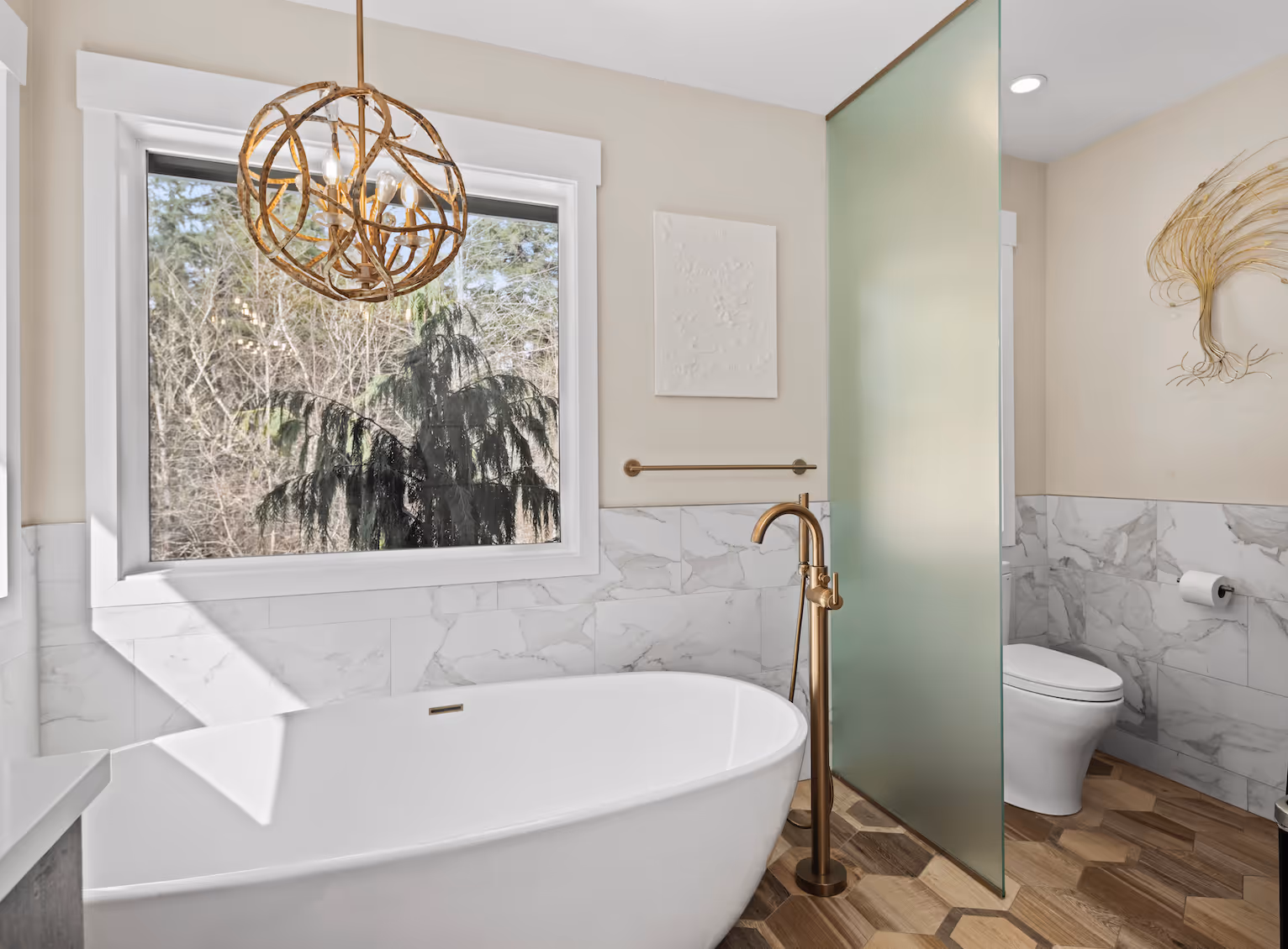 Modern bathroom with white freestanding tub, gold fixtures, frosted glass partition, and wood-patterned floor.