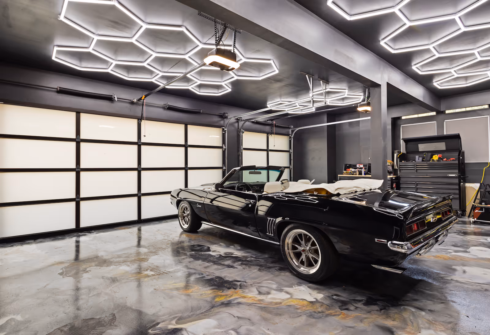 Black vintage convertible Camaro parked in a modern garage with hexagonal ceiling lights.
