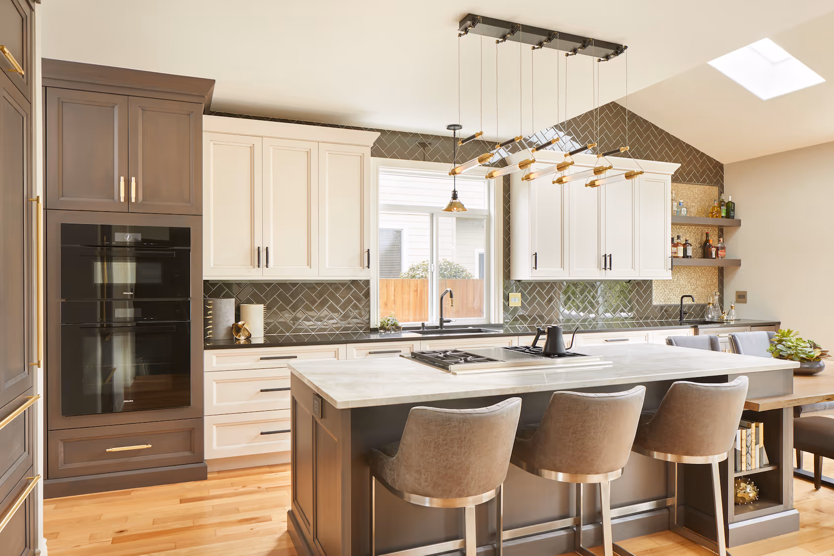 Modern kitchen with gray and white cabinets, marble island, gray chairs, and stylish hanging light fixture.