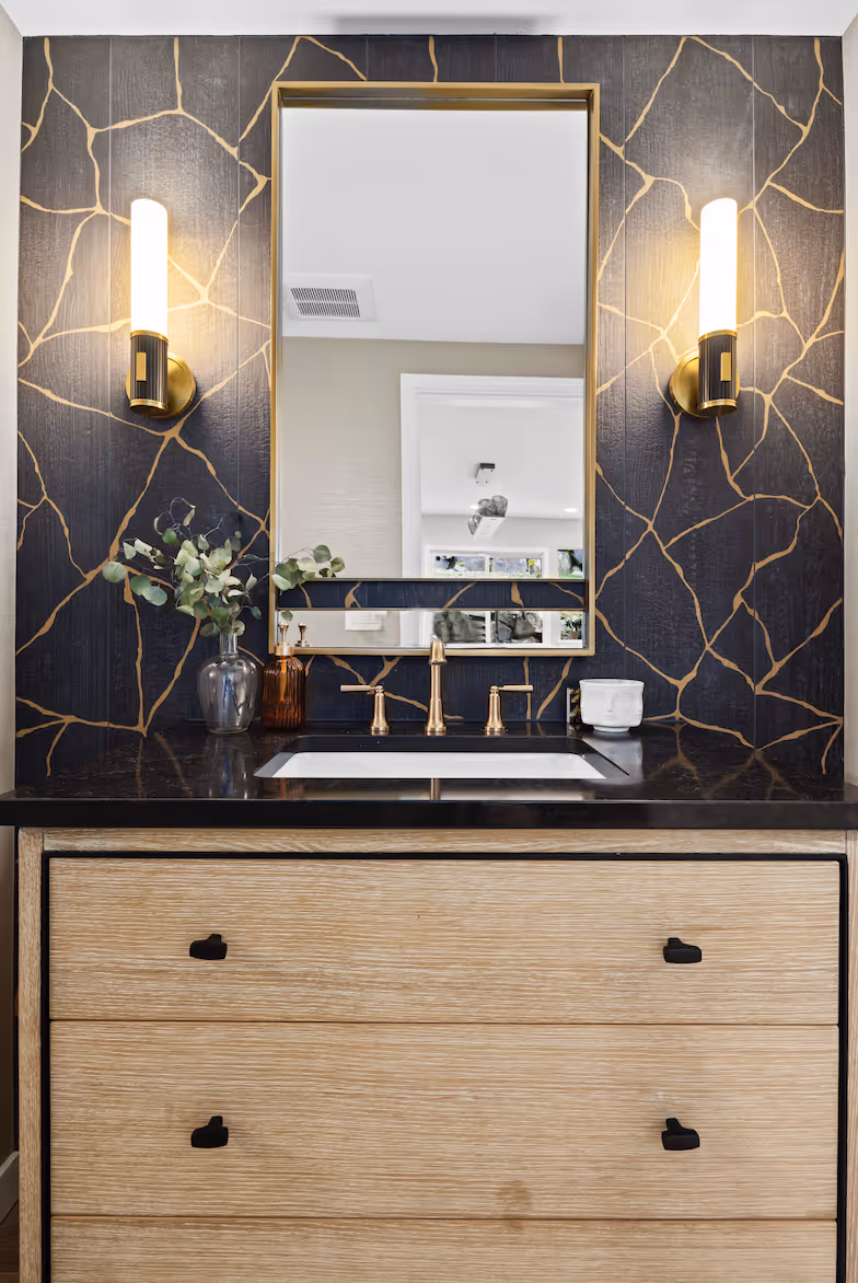 Modern bathroom vanity with black countertop, gold faucet, rectangular mirror, and patterned wall lights.