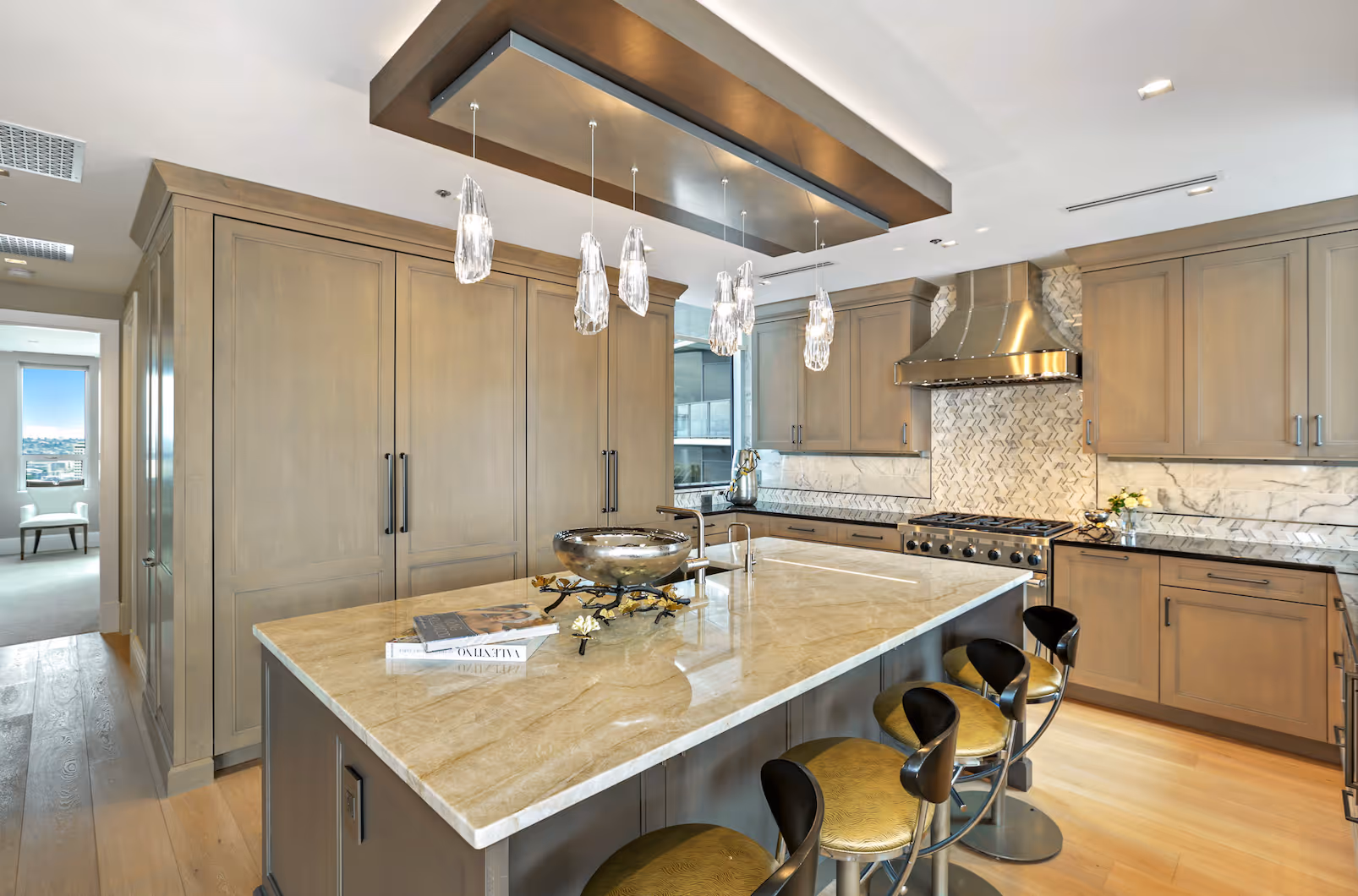 Modern kitchen with marble island, hanging crystal lights, wooden cabinets, and stainless steel stove.