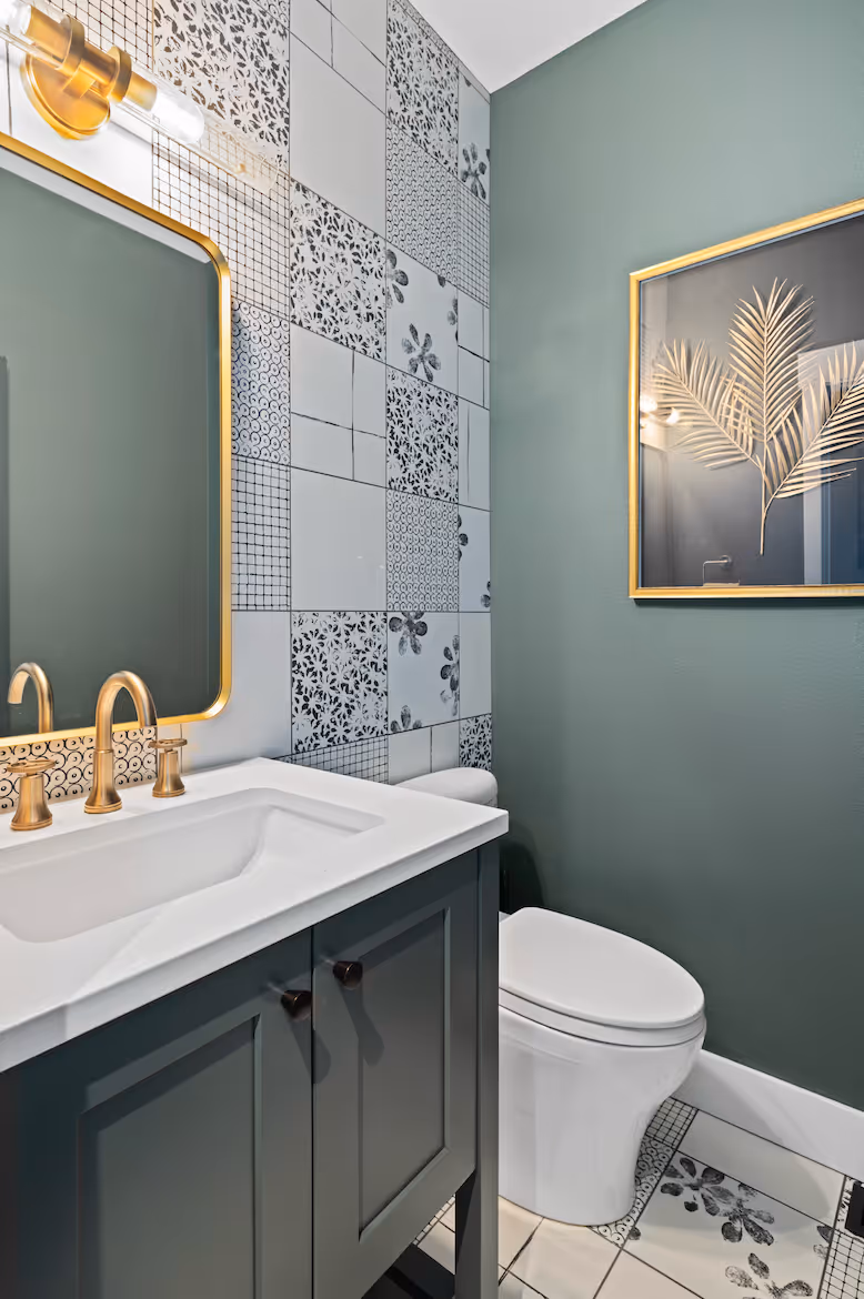 Modern bathroom with patterned tiles, green walls, gold-framed mirror and faucet, and white toilet.