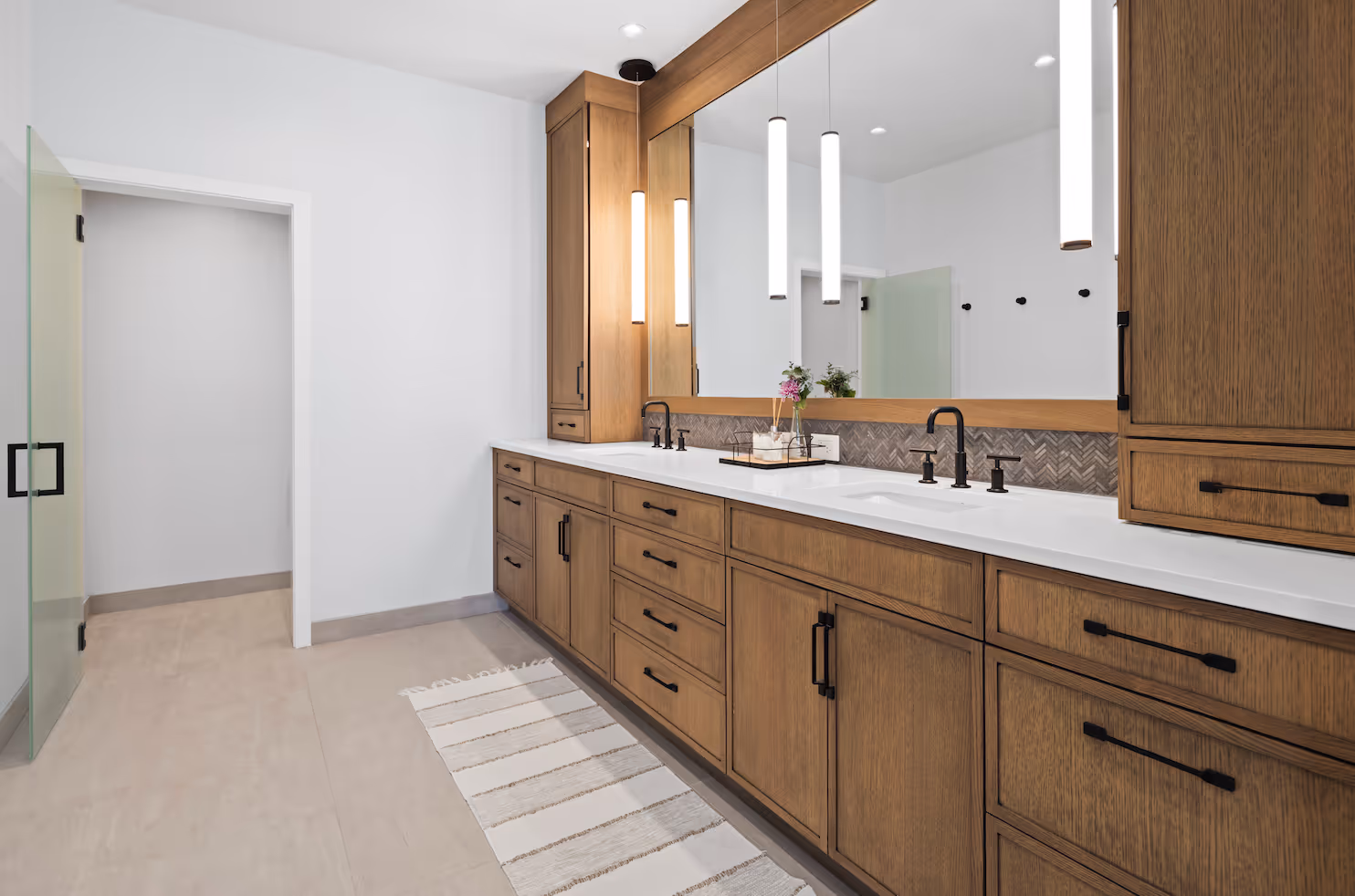 Modern bathroom with double sinks, large mirror, wood cabinets, and pendant lights over countertop.