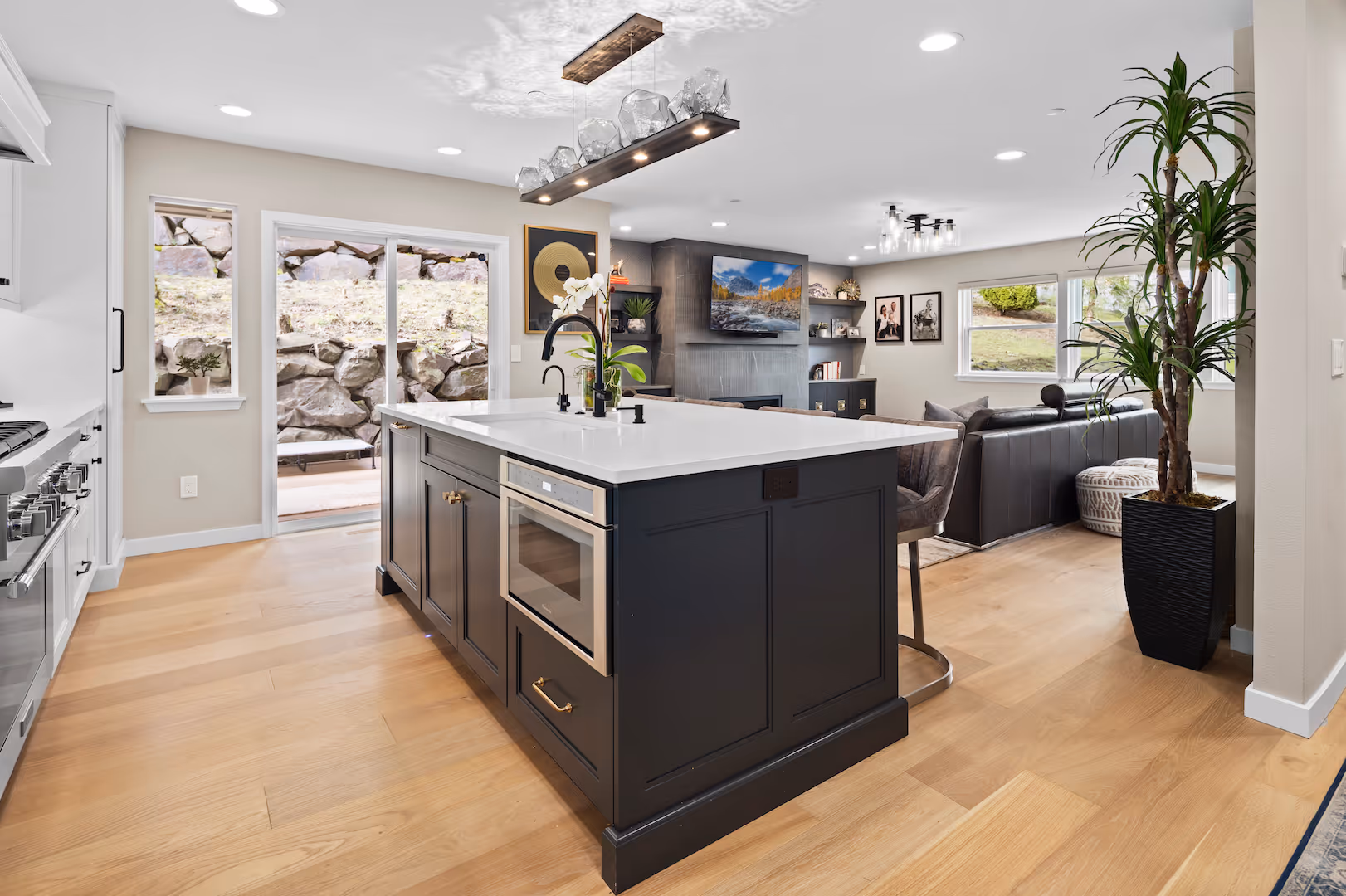 Modern kitchen with black island, white countertop, wood floors, and a view into a living room area.