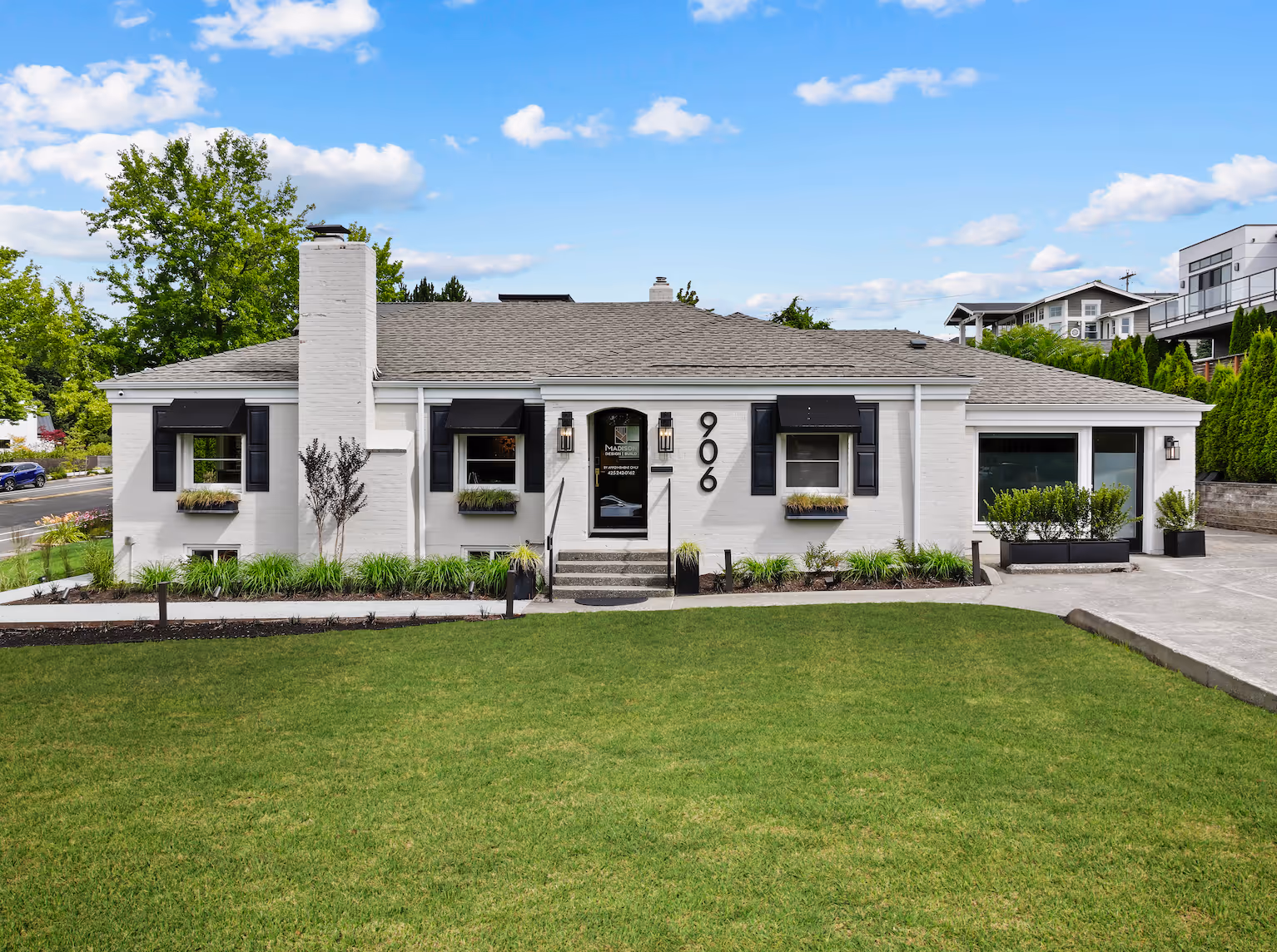 White brick house with black shutters, three front windows, green lawn, and the number 906 on the wall.