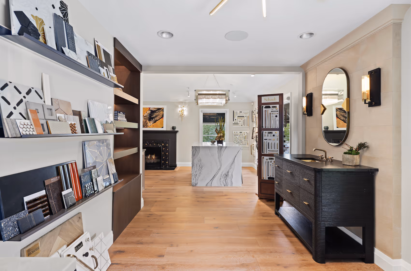 Interior showroom with wood floors, marble island, tile samples on the left, and black vanity with mirror on right.
