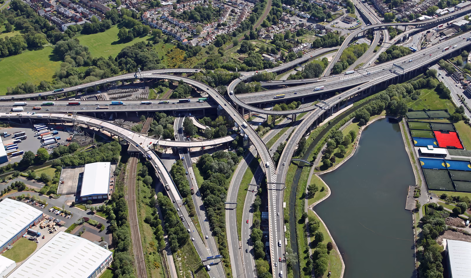 Aerial view of a large multi-level highway interchange with surrounding greenery, water, and buildings.