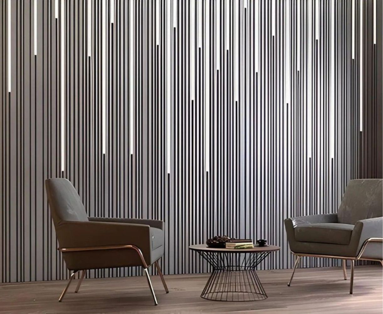 Two gray armchairs with metal legs facing a round wireframe coffee table in front of a vertical striped wall panel.