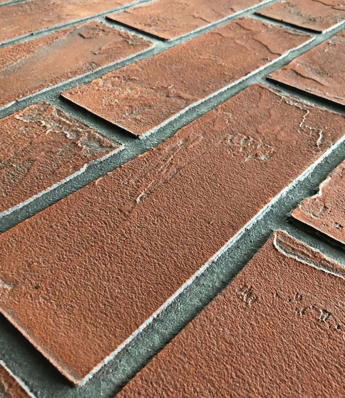 Close-up of textured reddish-brown rectangular tiles laid with gray grout in a staggered pattern.