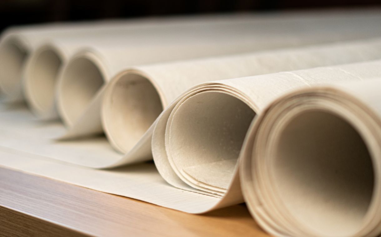 Close-up of several rolled white paper sheets on a wooden surface.