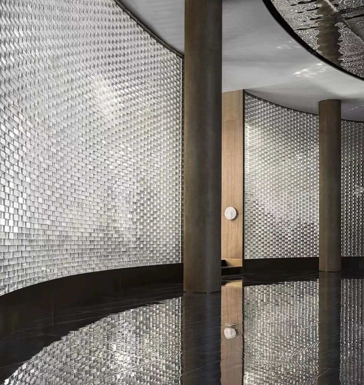 Curved interior wall with reflective glass blocks, tall columns, and shiny black floor reflecting light.