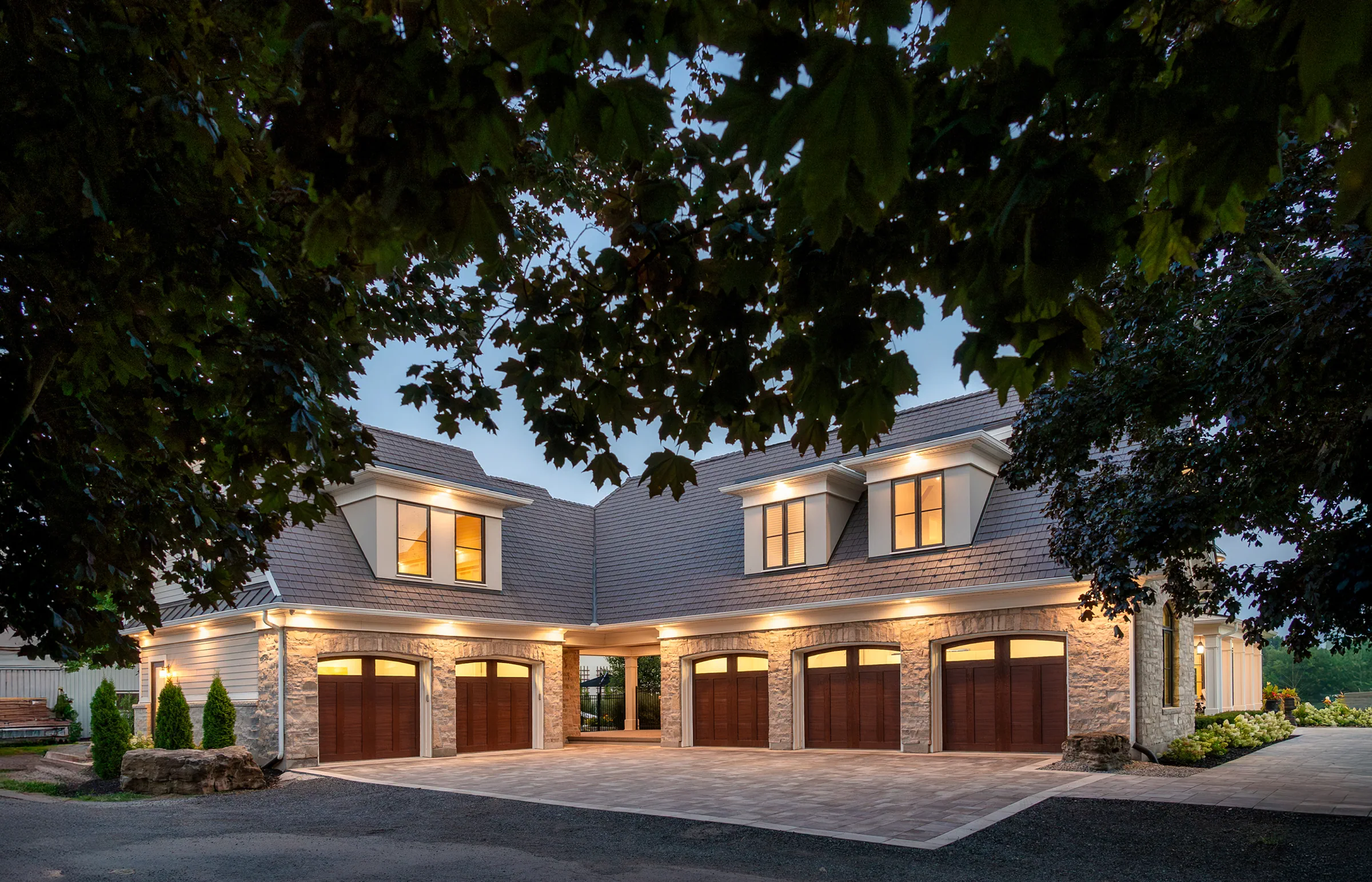 Stone garage at dusk with a grey roof, four dormers and illuminated wooden doors.