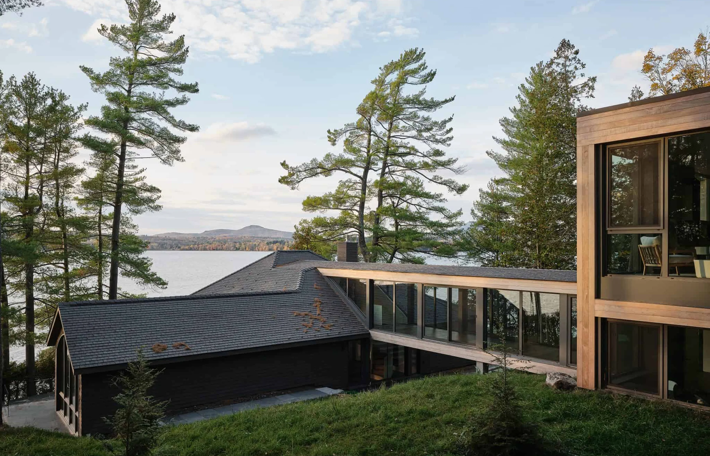 Modern lakeside home with a dark pitched roof connected to a wood-clad wing by a glass corridor.