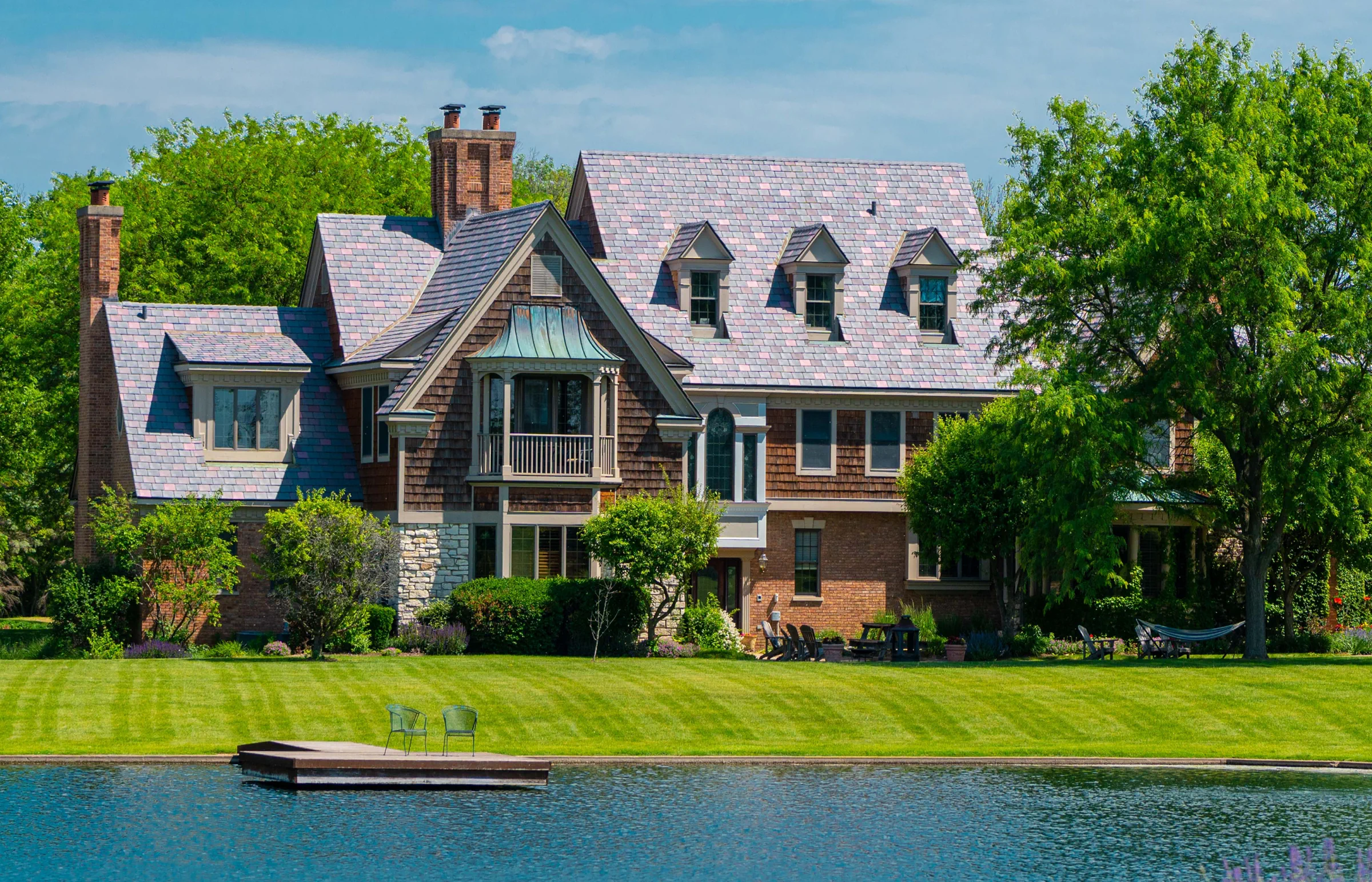 Lakeside home with a multi-tone slate-style roof, three dormers and brick chimneys.