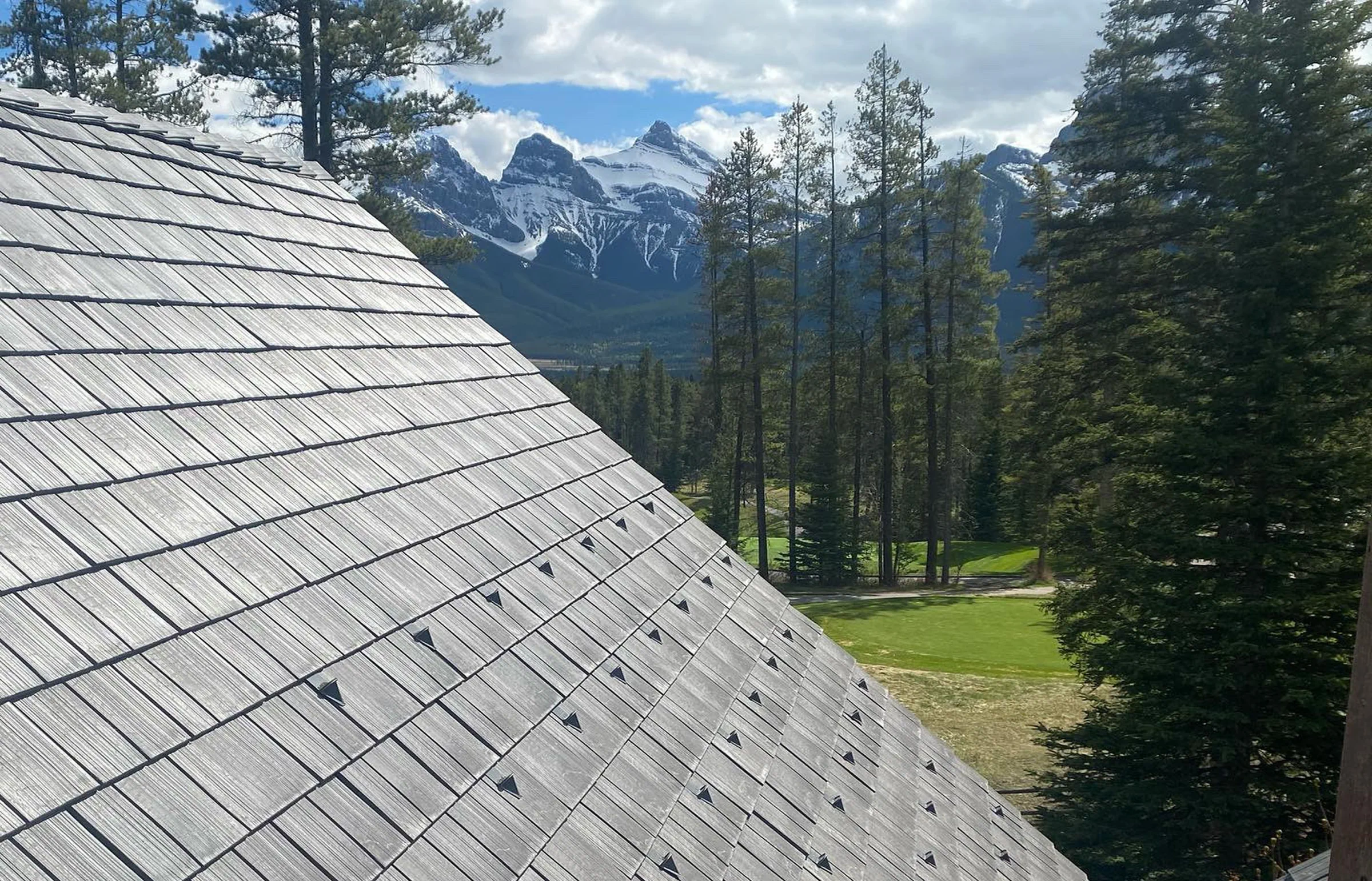 Close-up of a grey shake-style roof fitted with snow guards against a mountain backdrop.