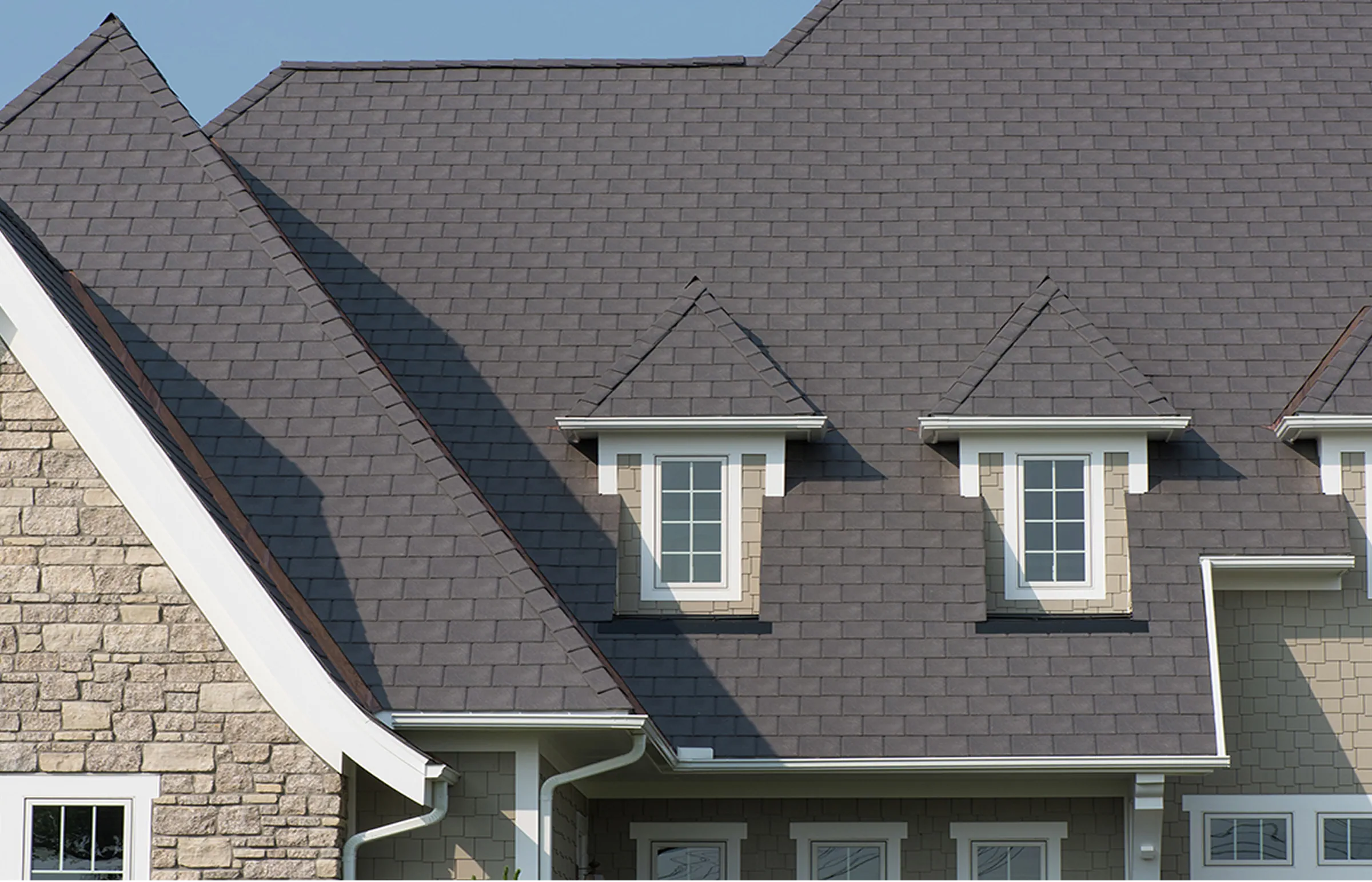 Grey slate-style roof with two dormer windows beside a stone gable.