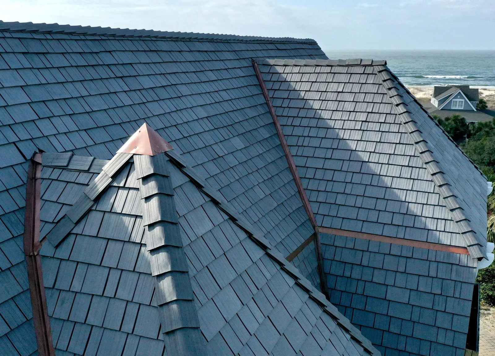 Grey shake-style roof with copper valleys and a pointed turret beside the ocean.