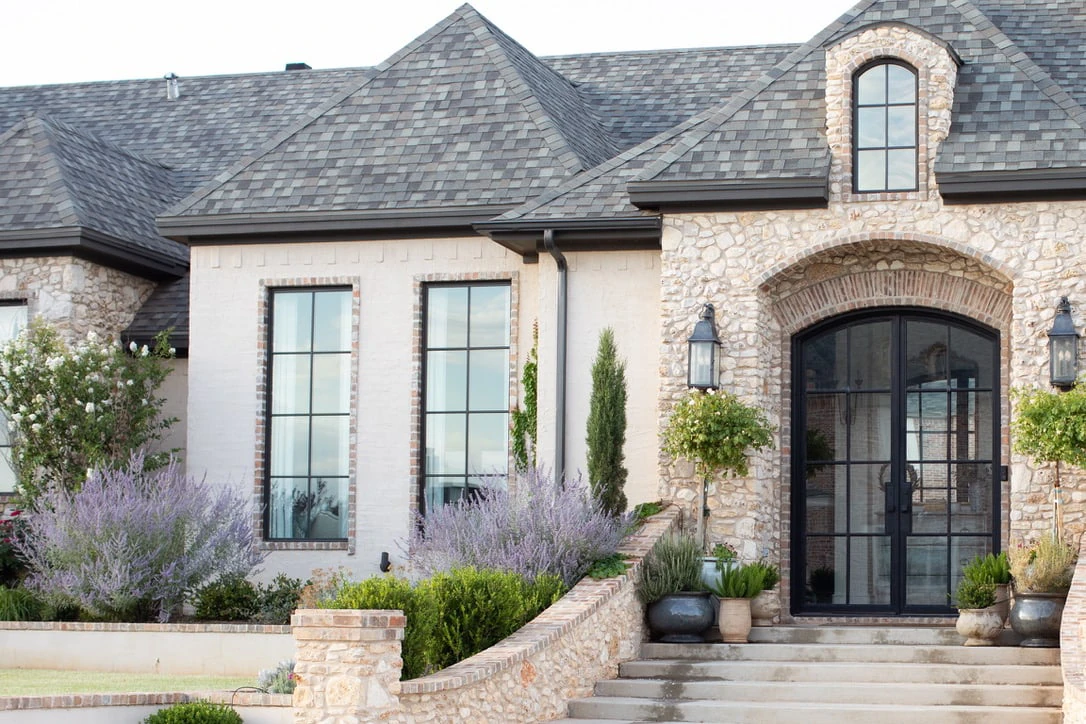 Roof comparison showing grey asphalt shingles on the same stone and stucco home.