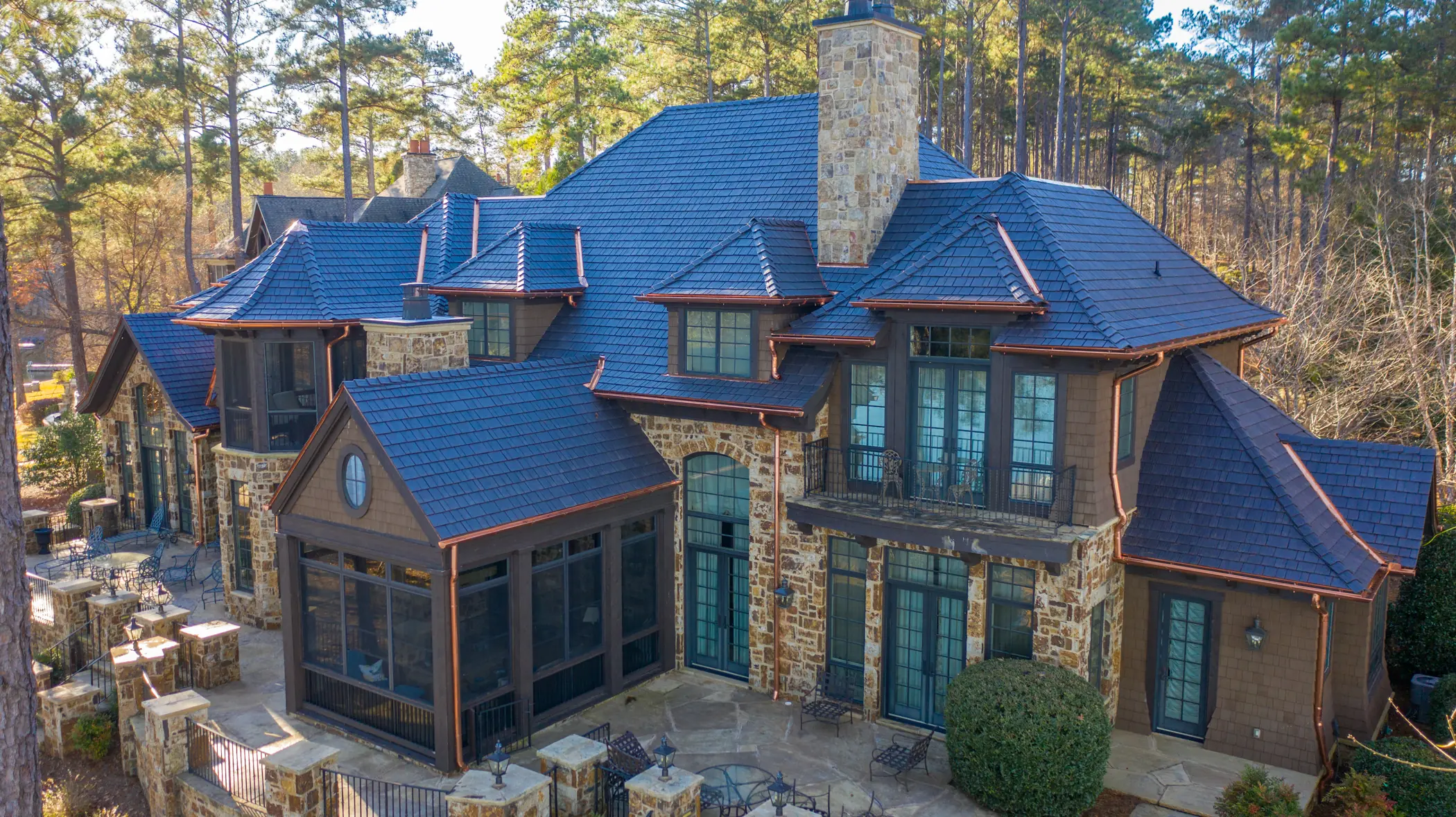 Aerial view of an Enviroshake roof with multiple gables, copper trim and a central stone chimney.