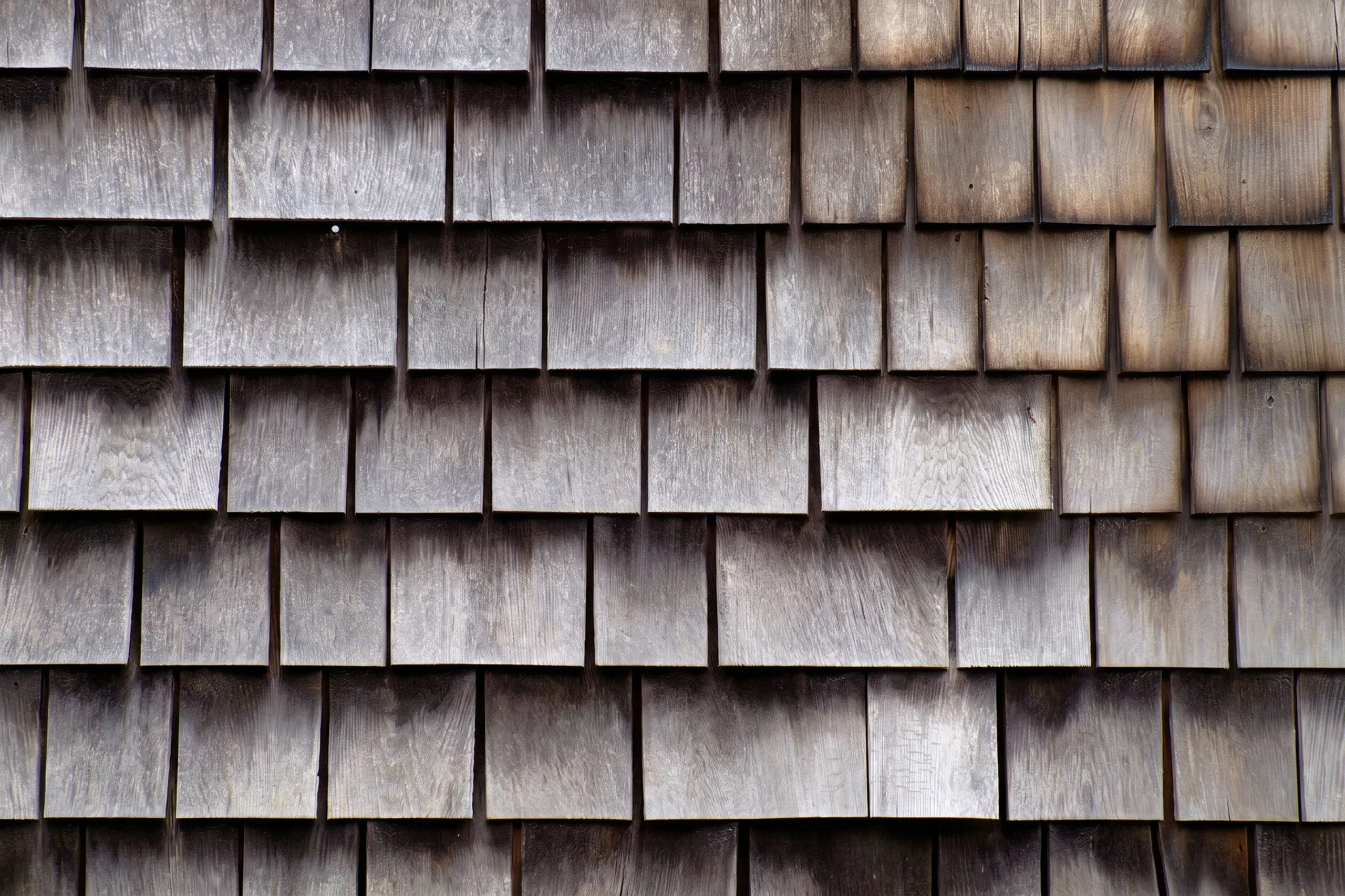 Close-up of weathered cedar shake shingles with dark fire damage streaking across the surface