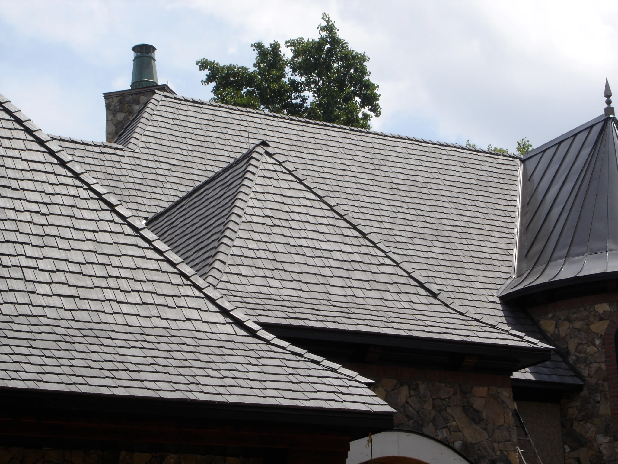 Aged Cedar Enviroshake composite cedar shake roofing on a large home with multiple rooflines and stone exterior.