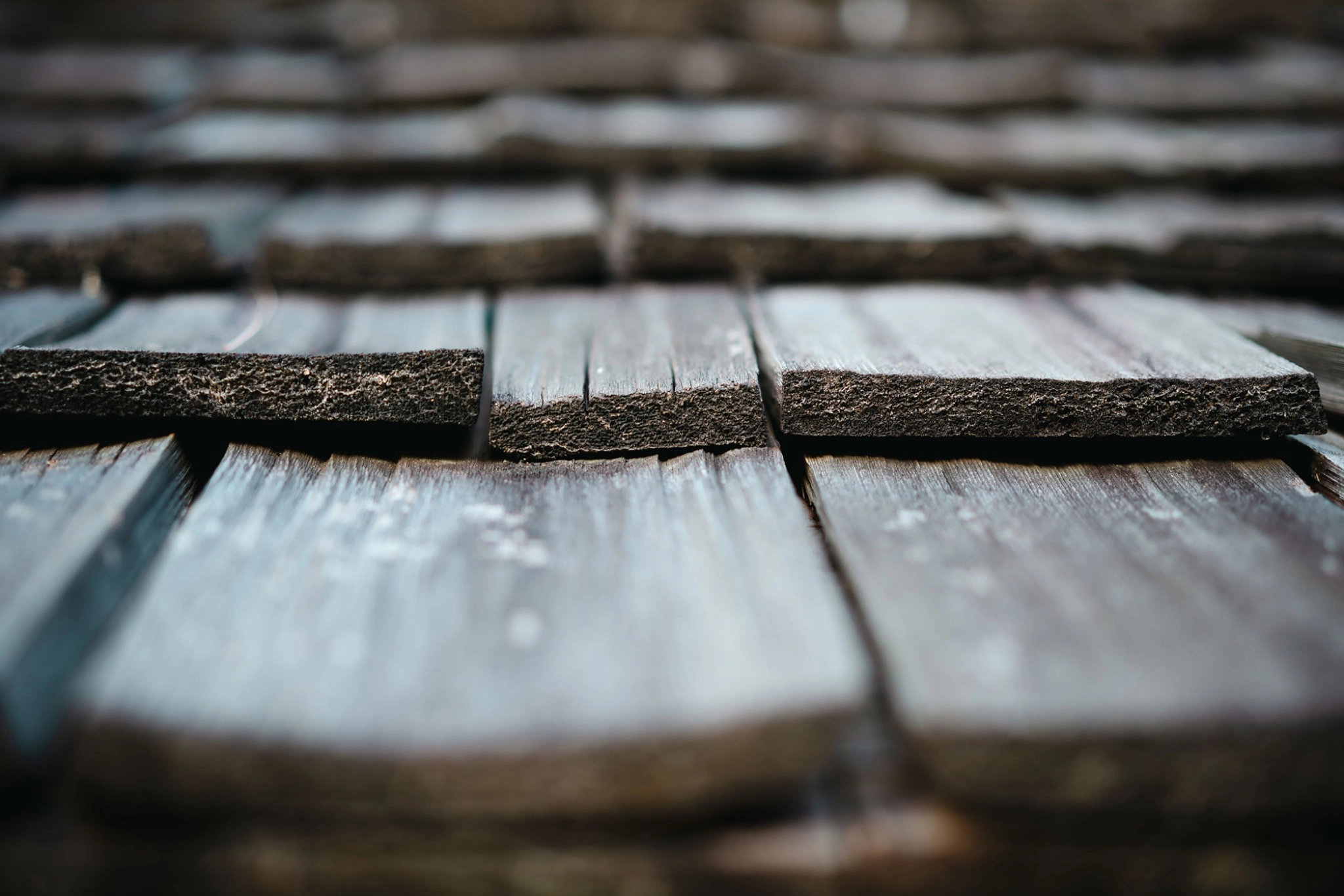 Close-up of weathered wood shake roofing, showing natural graining, texture, and slight warping from age.