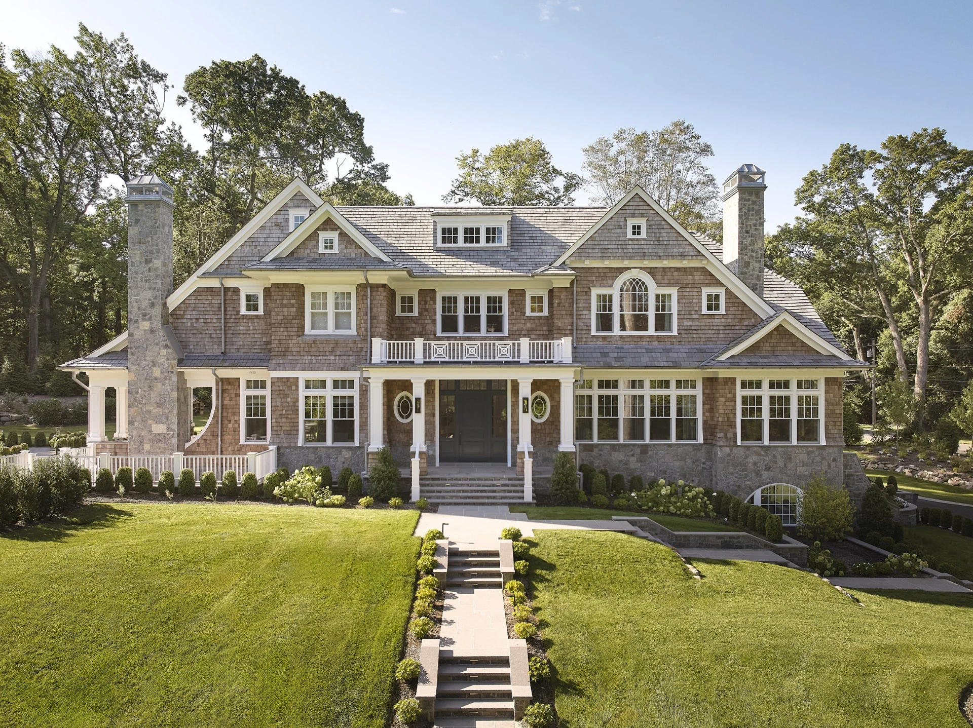 Large shingle-style home with a gray Enviroshake composite roof, cedar shake siding, stone chimneys, and a grand front lawn with landscaped pathway.