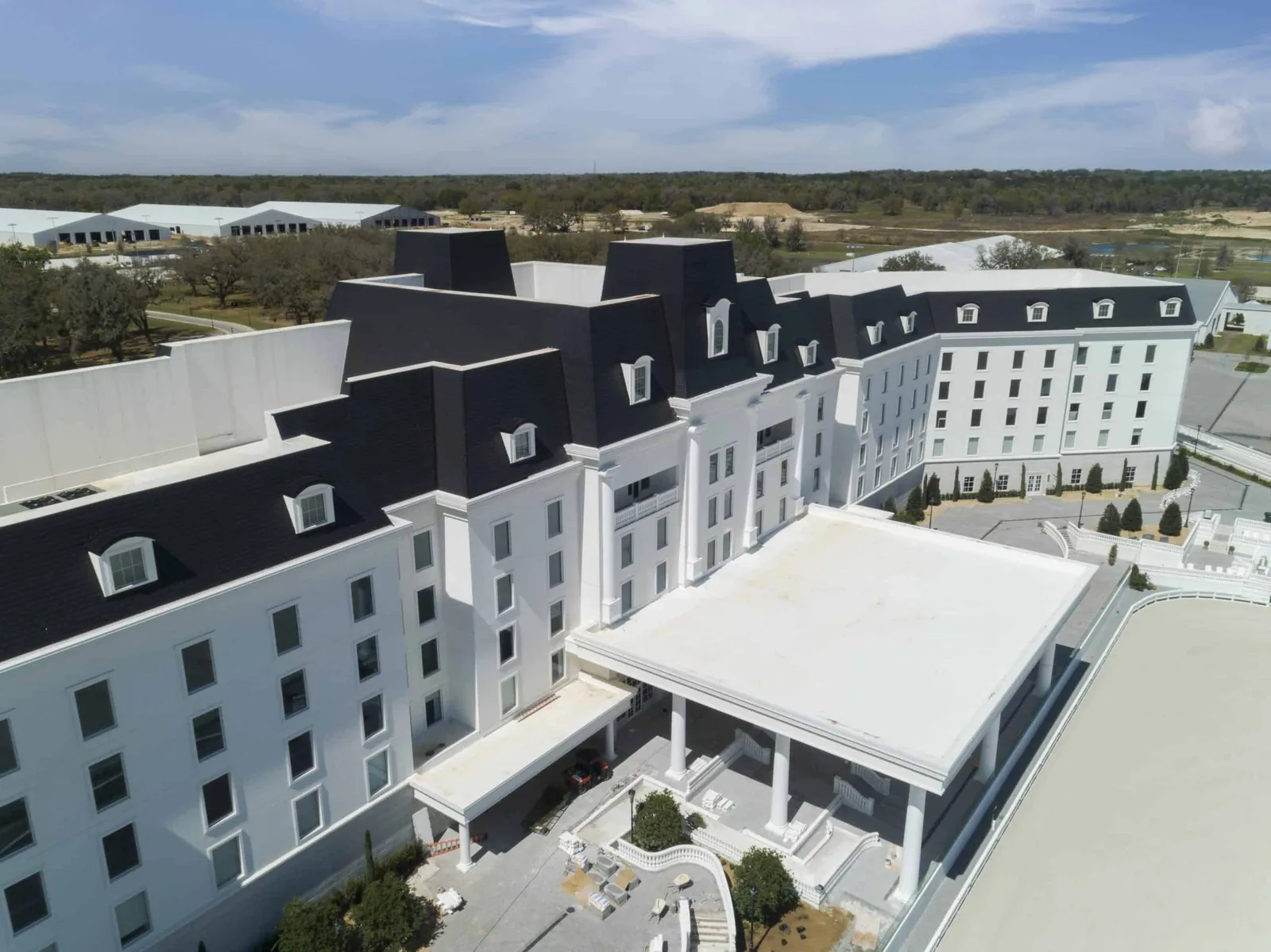 Large white commercial building with a black Enviroslate composite slate mansard roof, multiple dormer windows, and a grand columned entrance overlooking an equestrian arena