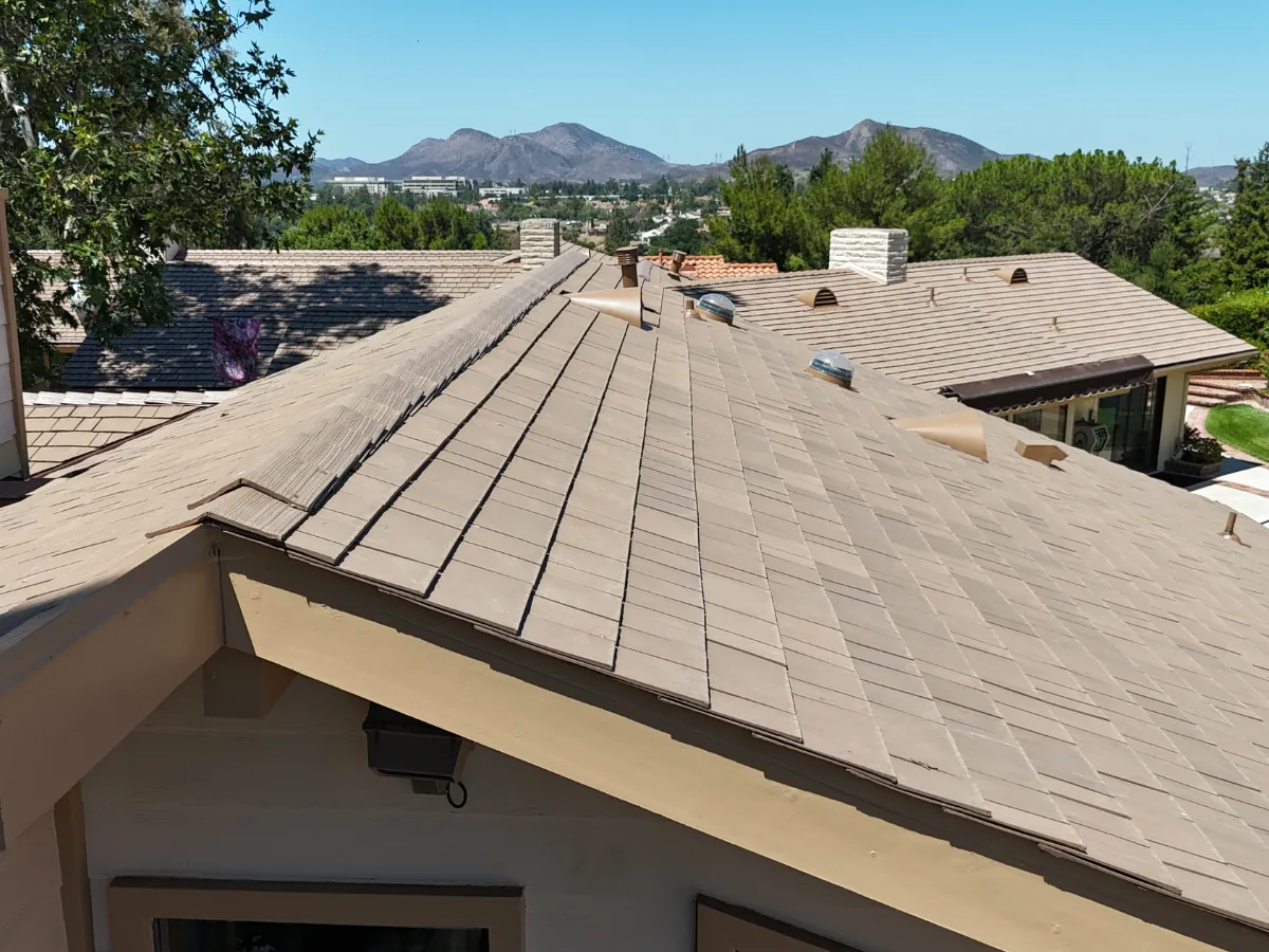Close-up view across a brown Enviroshake composite roof with roof vents, overlooking a suburban neighborhood with mountains in the background