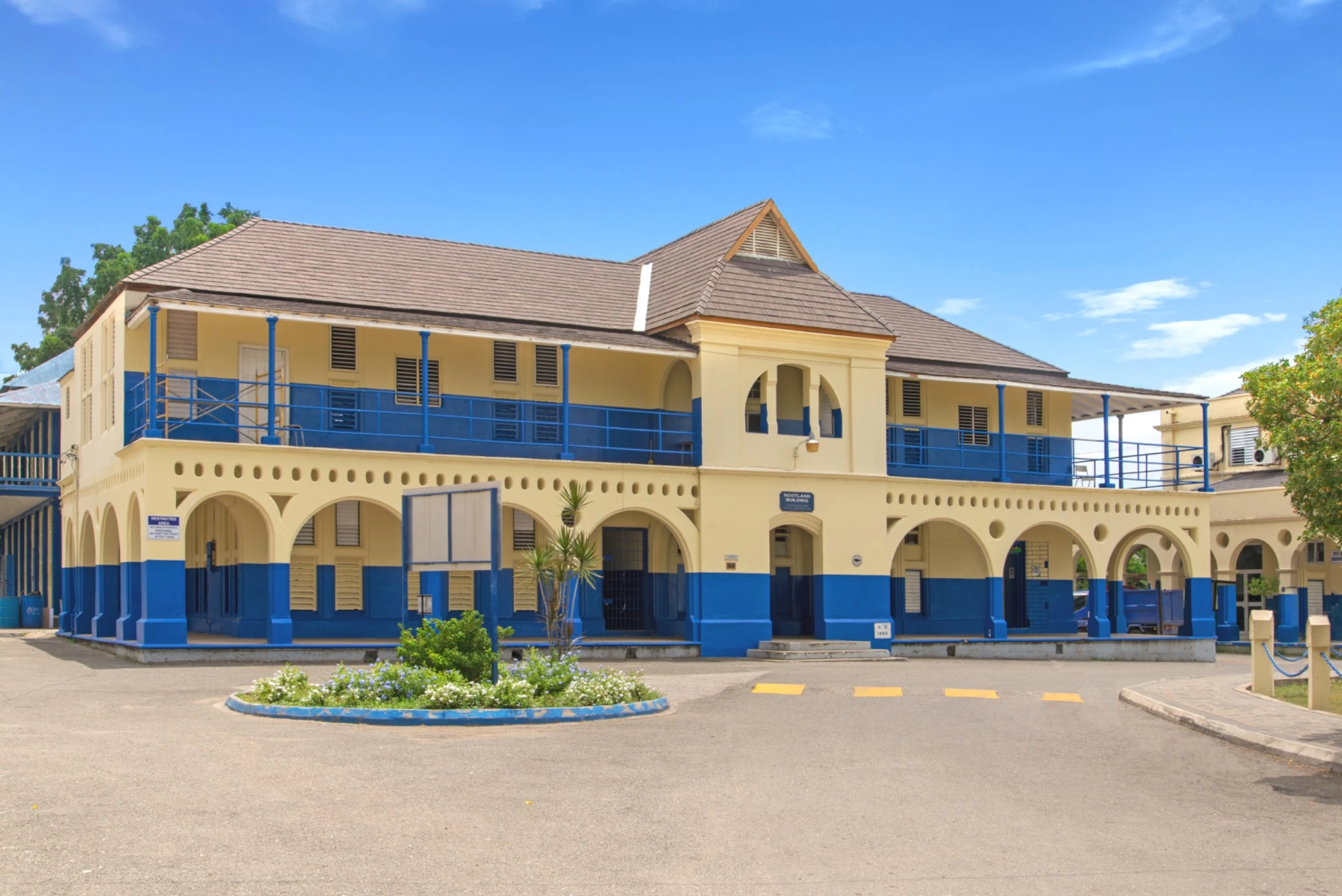 Historic two-story yellow and blue colonial-style school building with an aged cedar Enviroshake composite roof, arched arcade walkways, and a central bell tower,
