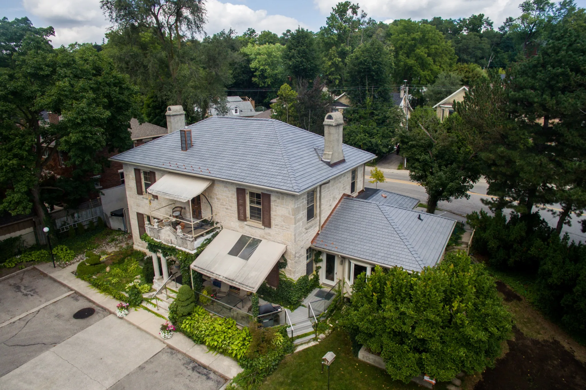 Silvered Cedar Enviroshake composite cedar shake roofing on a traditional stone home surrounded by mature trees and landscaping.