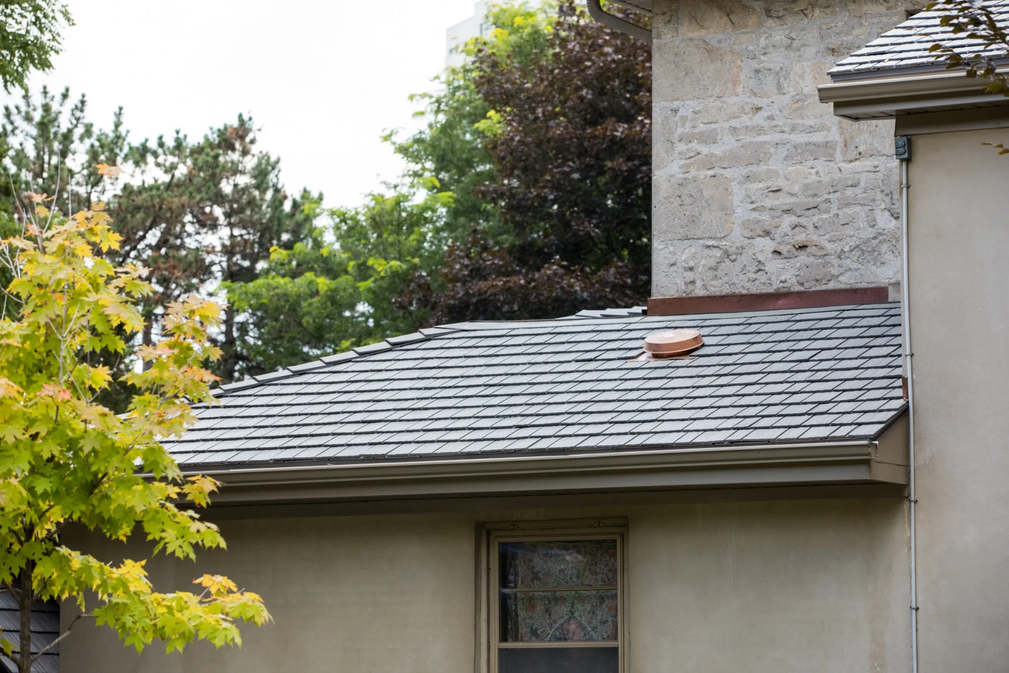 Silvered Cedar Enviroshake composite cedar shake roofing on a stone home surrounded by mature trees.