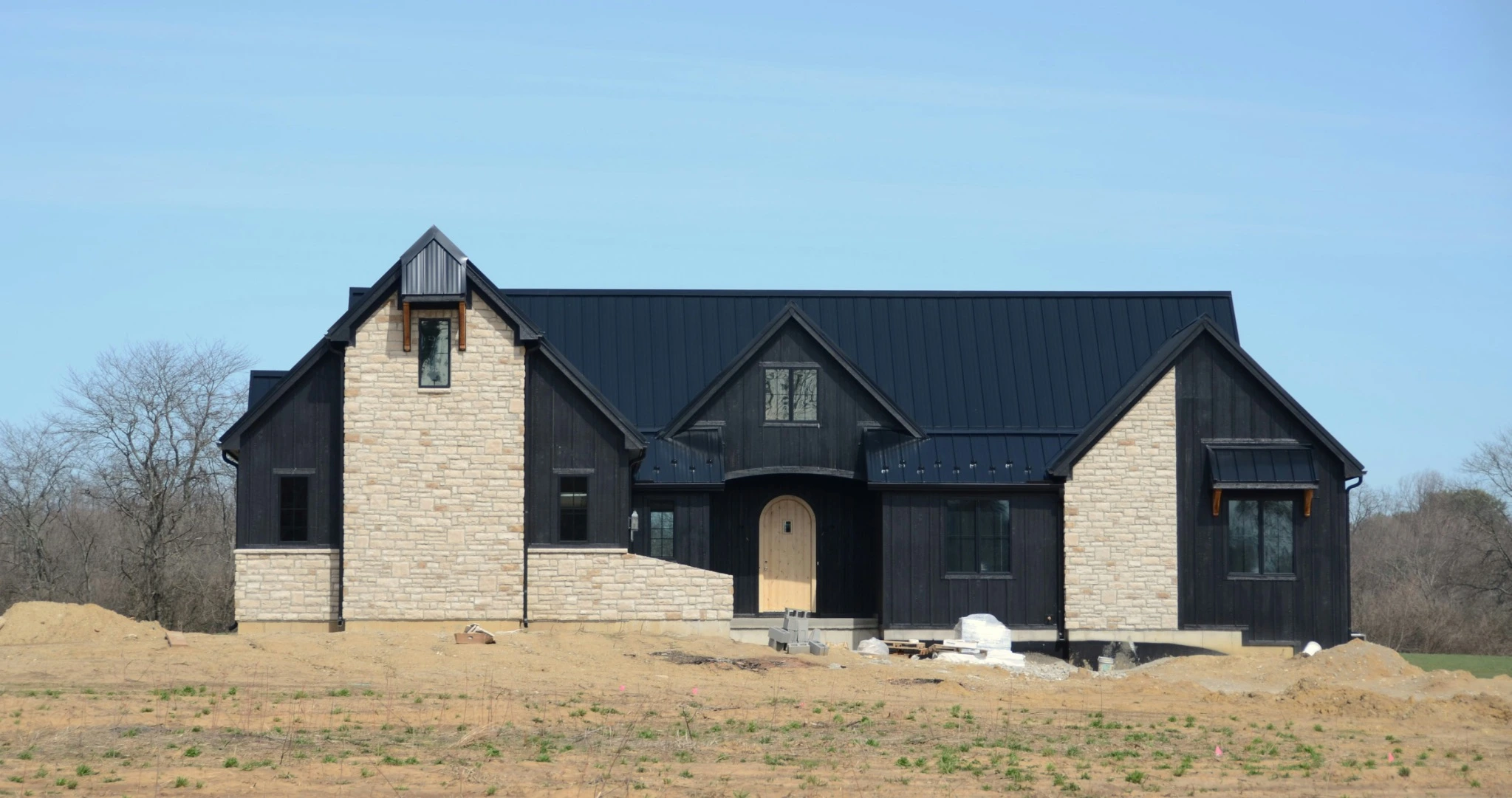 Black standing seam metal roofing on a contemporary home with dark siding and light stone accents.